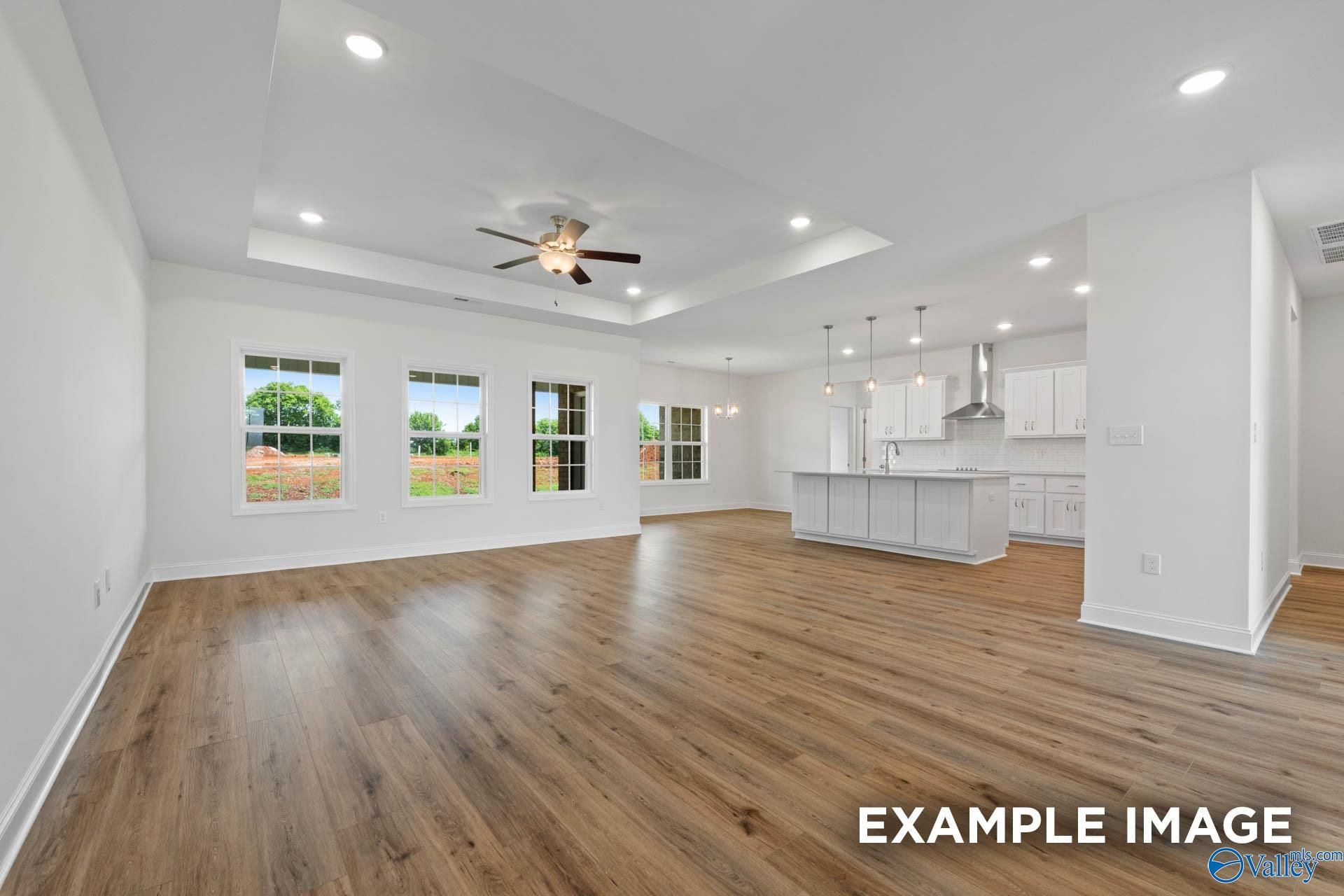 Open-concept living and kitchen with hardwood floors, large windows overlooking fields, white island, and ceiling fan in The Oxford by Davidson Homes, Huntsville