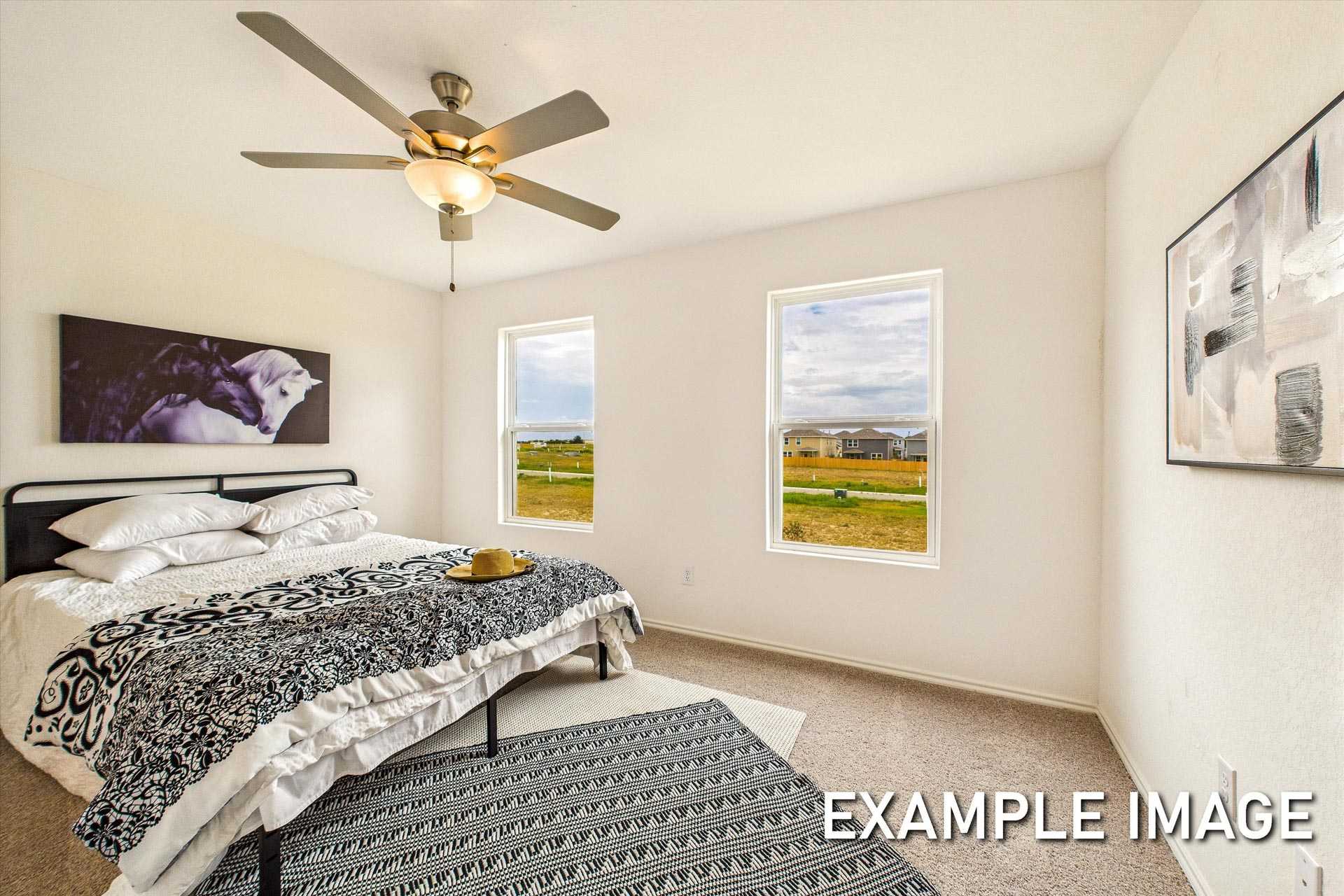 Spacious master suite in The Trinity B featuring king bed, ceiling fan, and large windows with scenic field views
