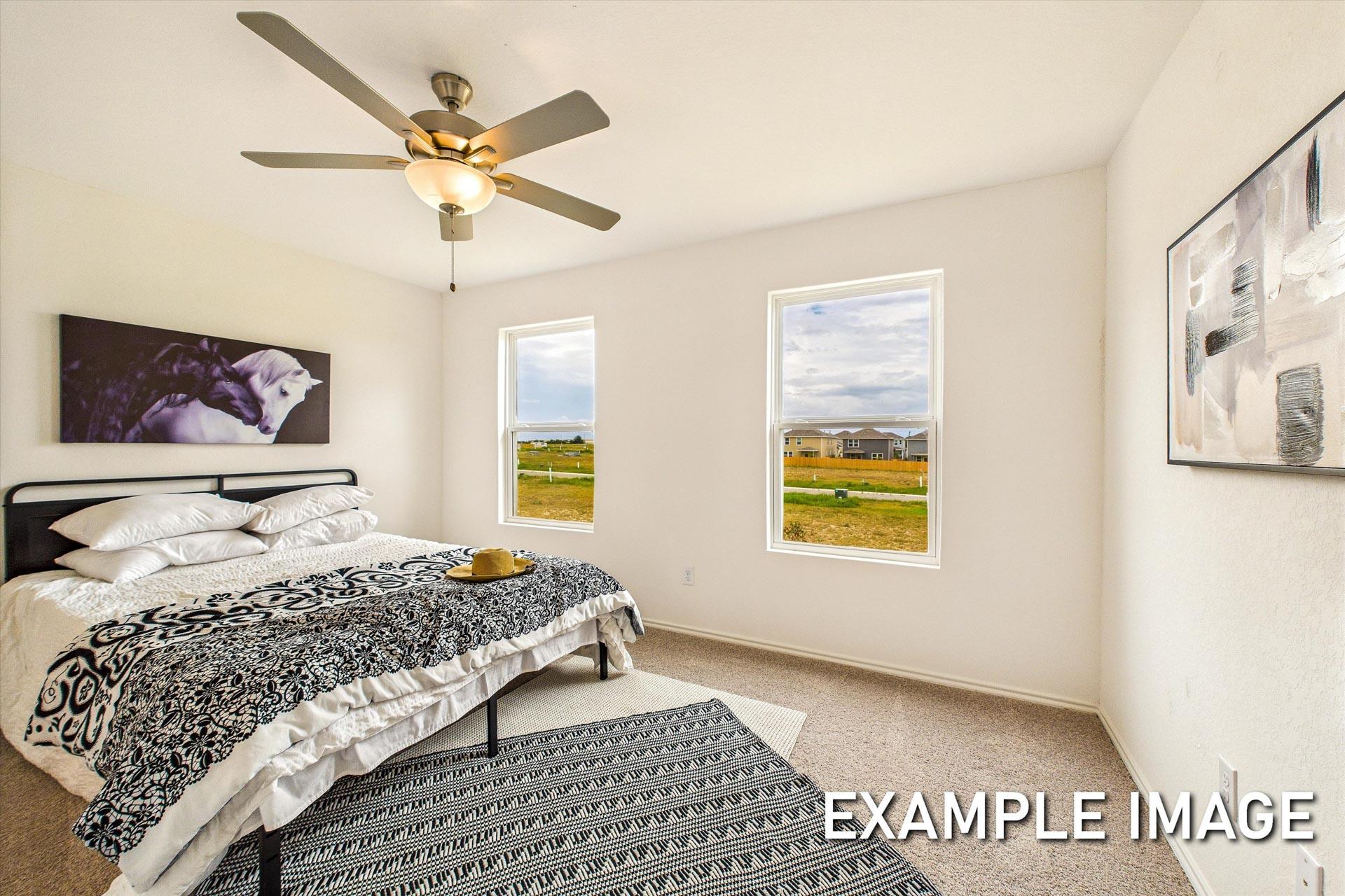 Spacious master suite in The Trinity B featuring king bed, ceiling fan, and large windows with scenic field views