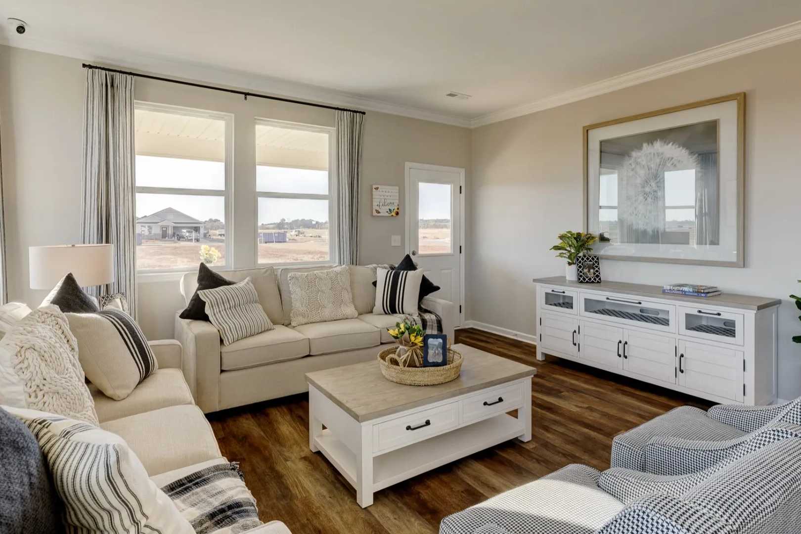 Inviting living room in The Aurora B with neutral tones, plush cream sofa, wooden coffee table, large windows, and potted plants