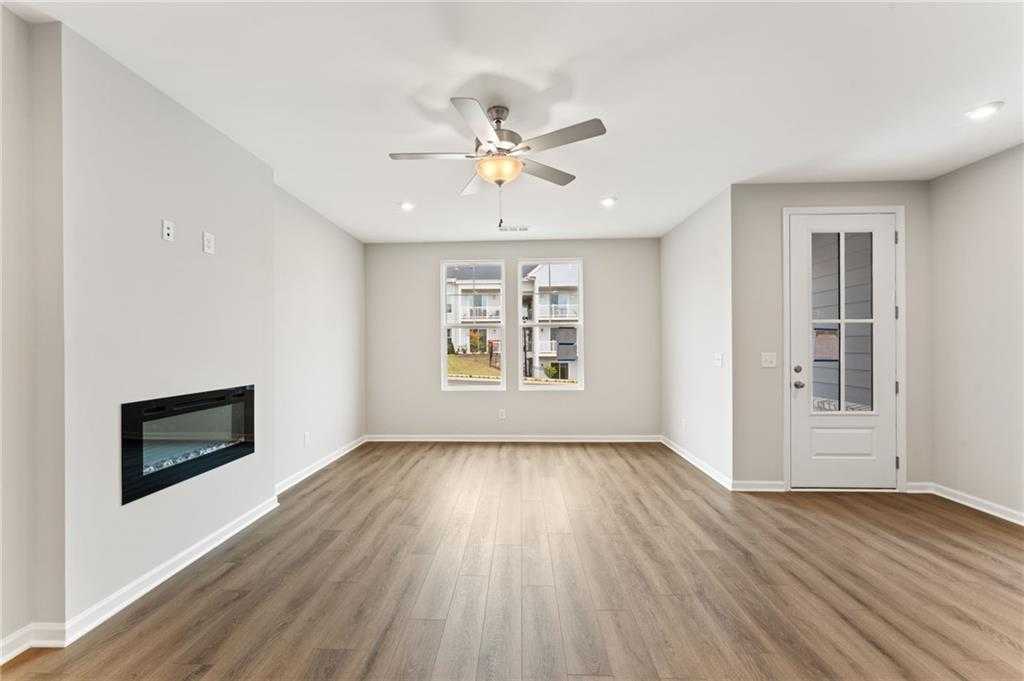 Bright living room with modern fireplace, hardwood floors, ceiling fan, and large windows in Davidson Homes The Monroe A, Emerson, Georgia