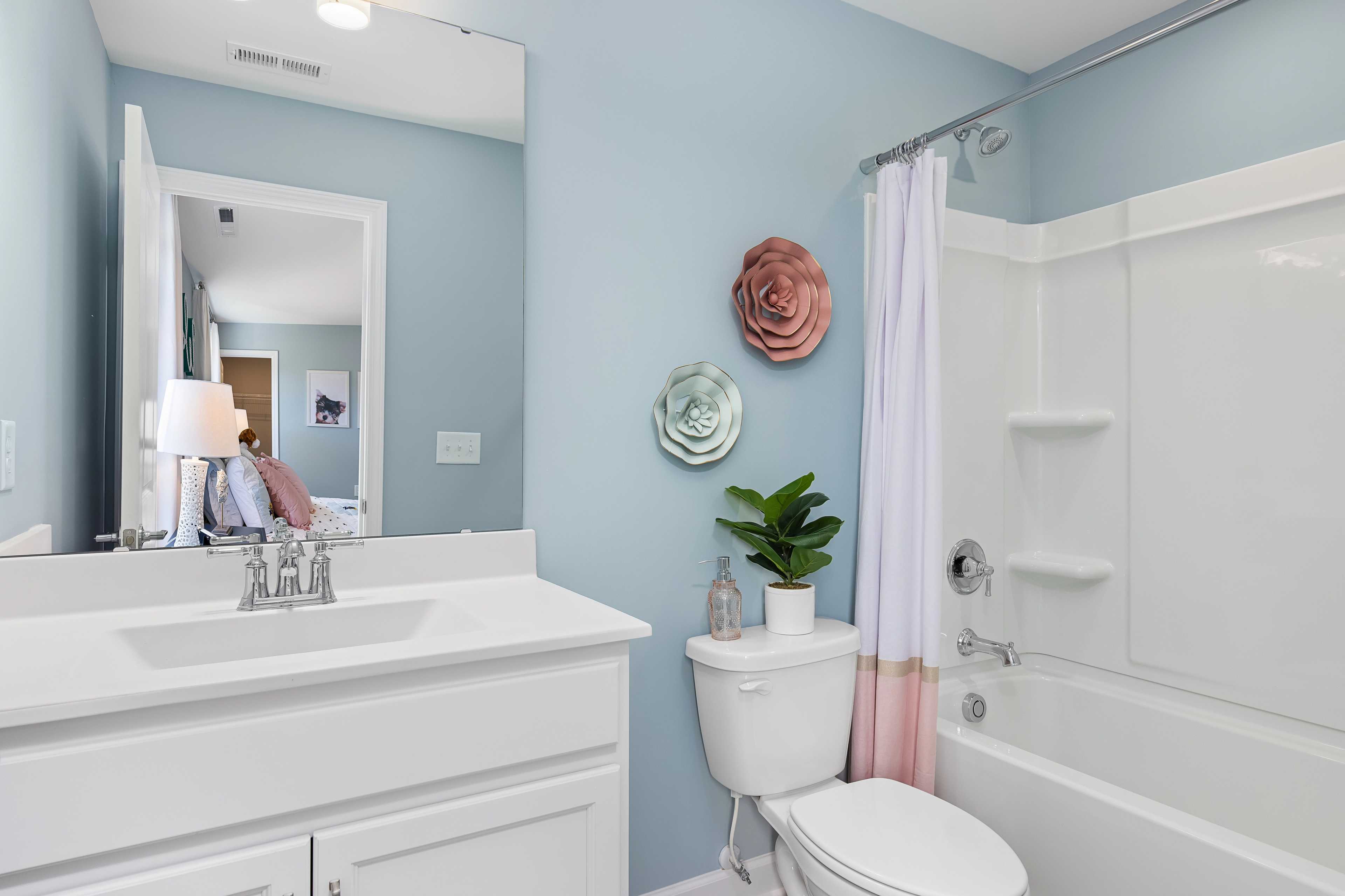 Spacious bathroom at Woodland Crossing in Zebulon NC with light blue walls pink floral decor white vanity and tub shower combo by Davidson Homes