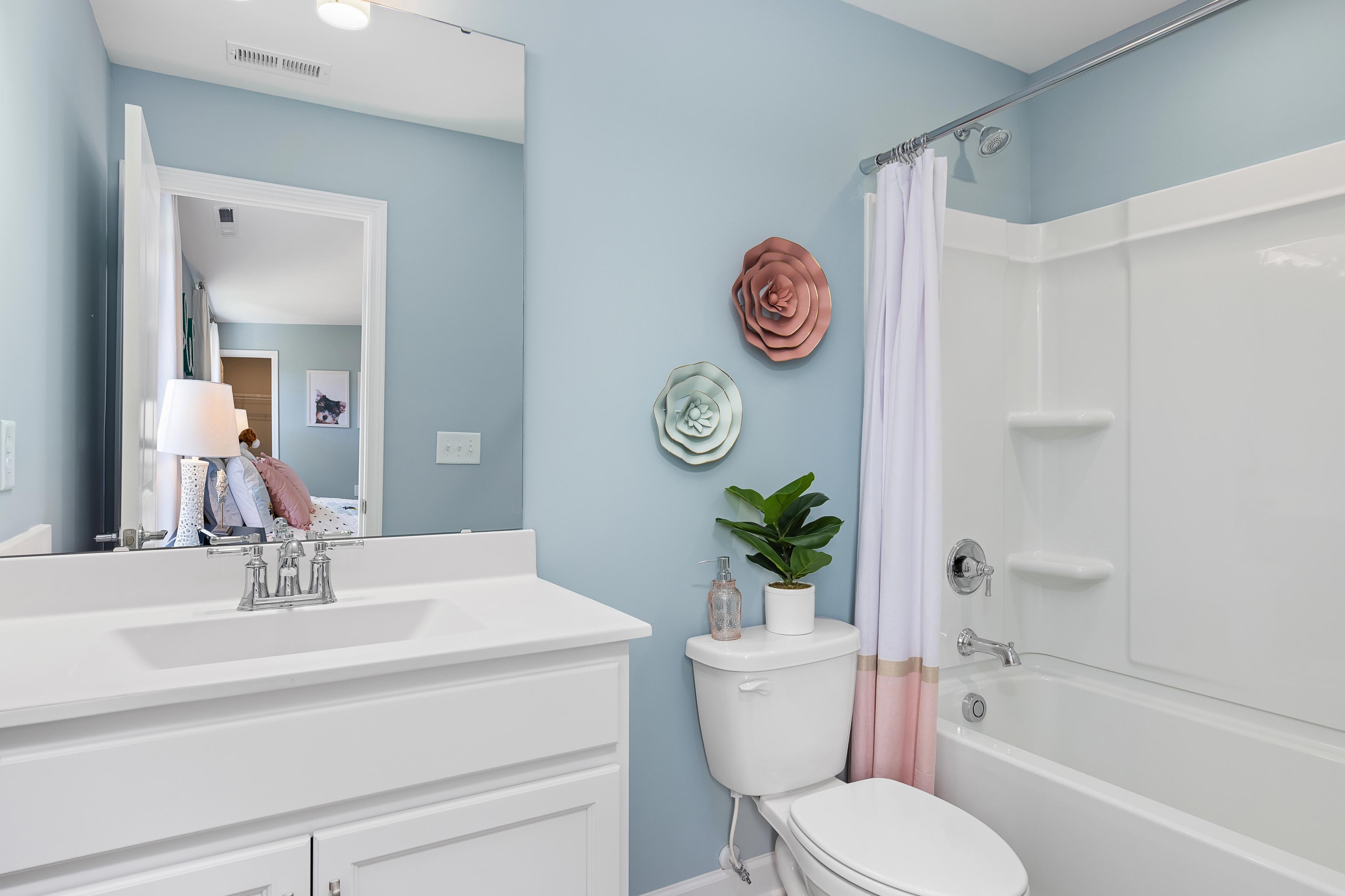 Spacious bathroom at Woodland Crossing in Zebulon NC with light blue walls pink floral decor white vanity and tub shower combo by Davidson Homes