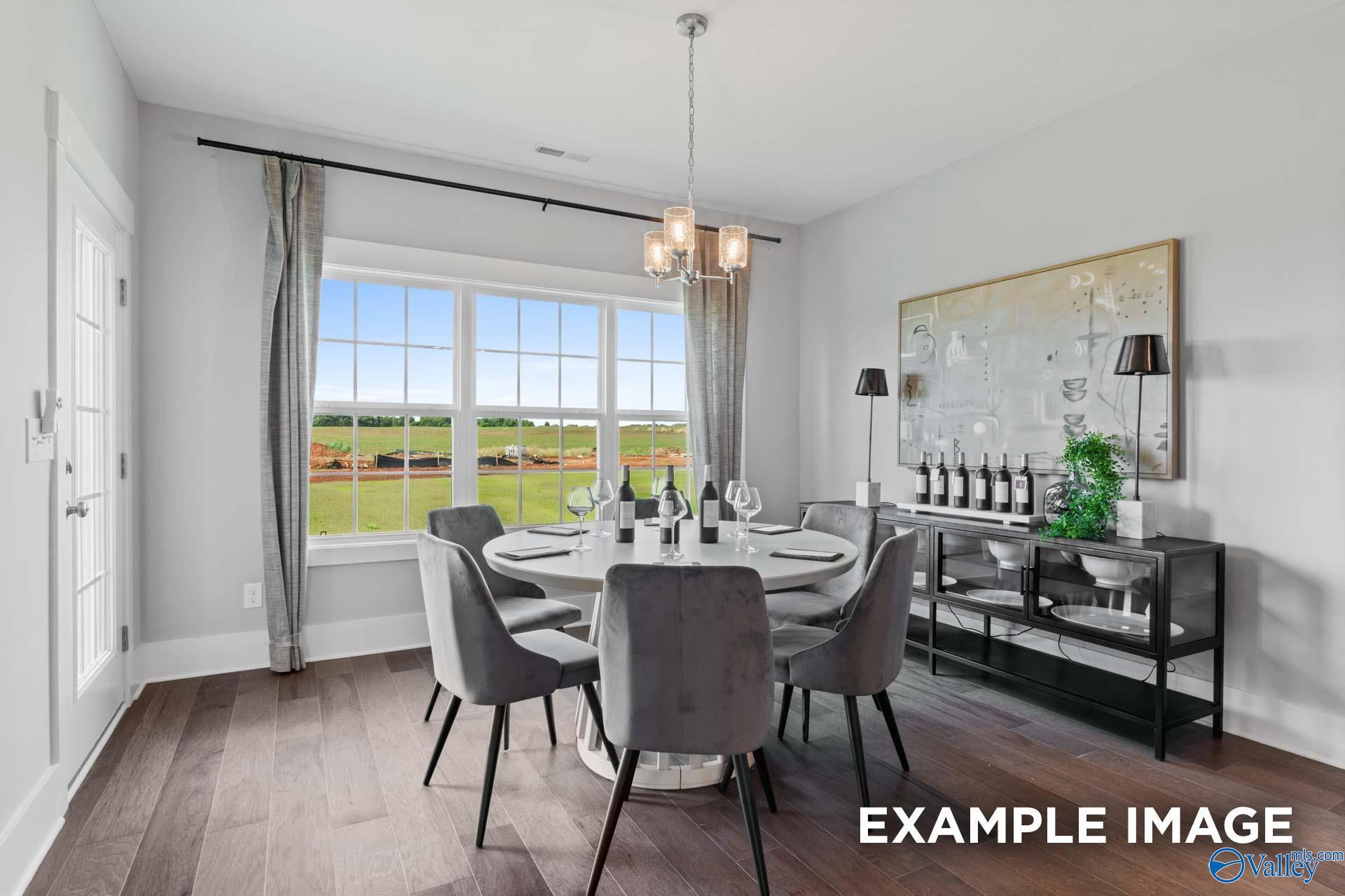 Elegant dining room with round gray table, chandelier, and scenic field view through large windows in The Finleigh, Huntsville, AL