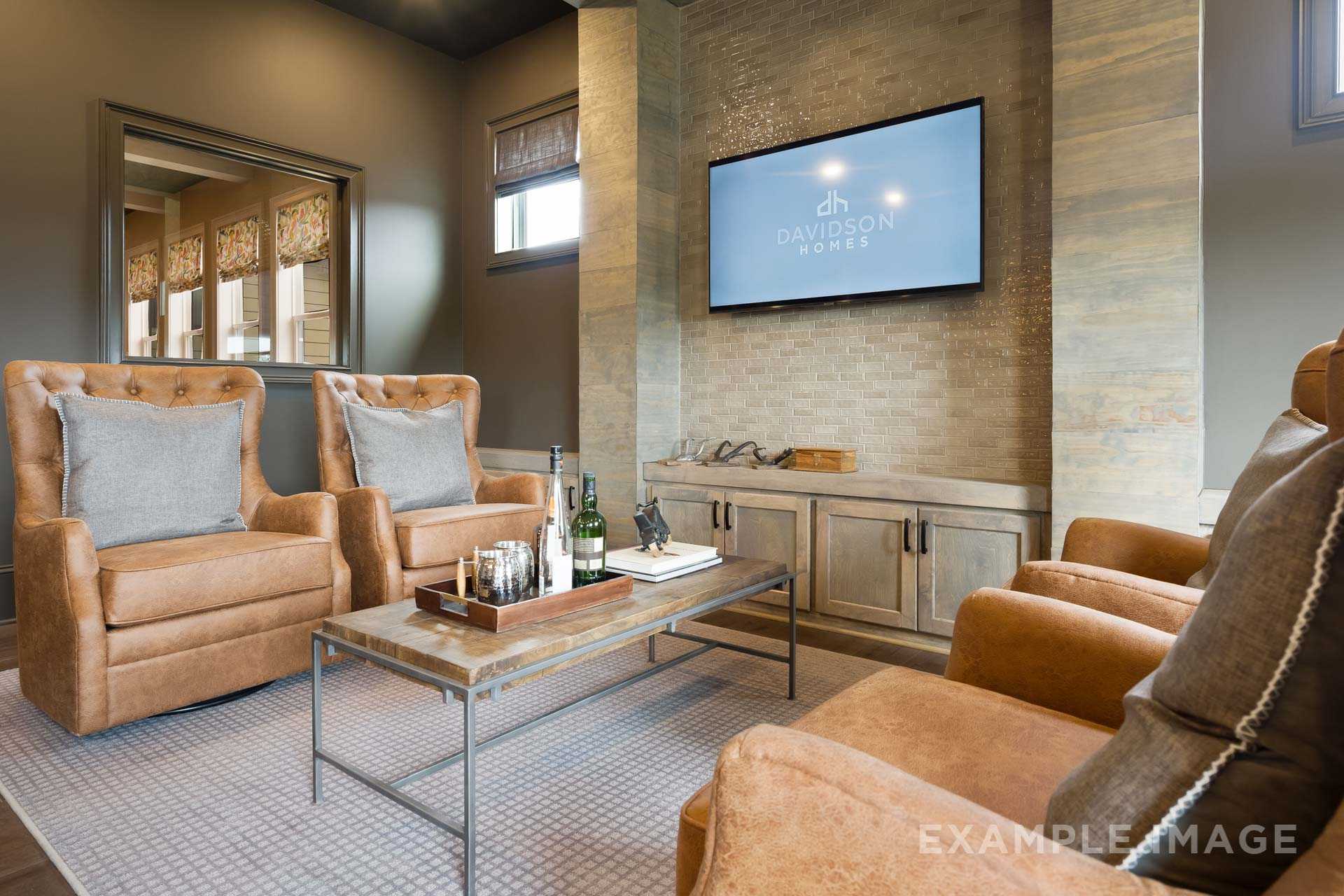Cozy media room in The Seaside by Davidson Homes featuring leather armchairs, entertainment wall with TV, and bar setup in Woodstock GA