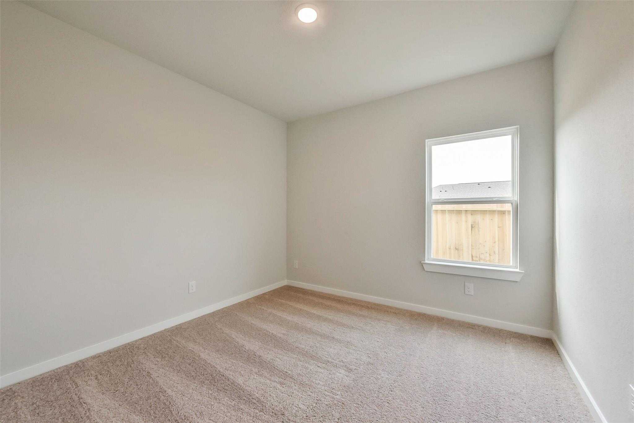 Bright secondary bedroom with beige carpet, large window overlooking fence in Davidson Homes The Frio G, Dayton, Texas