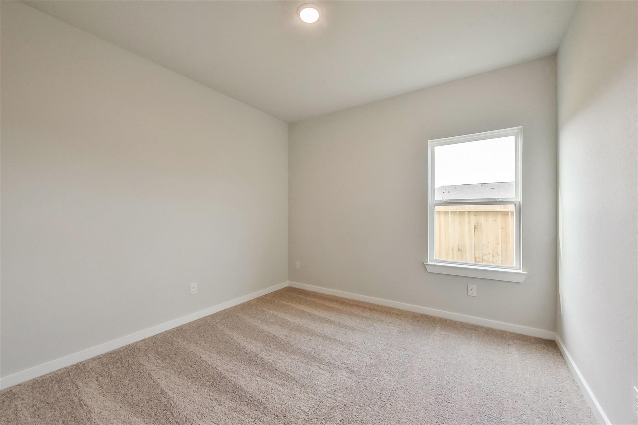 Empty secondary bedroom with neutral walls, carpeted floor, and window view of wooden fence in Davidson Homes The Frio G, Dayton Texas