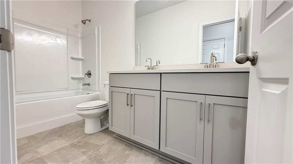 Modern guest bathroom with grey vanity and tub-shower combo in The Glenwood A floor plan at Wehunt Meadows, Hoschton, GA.