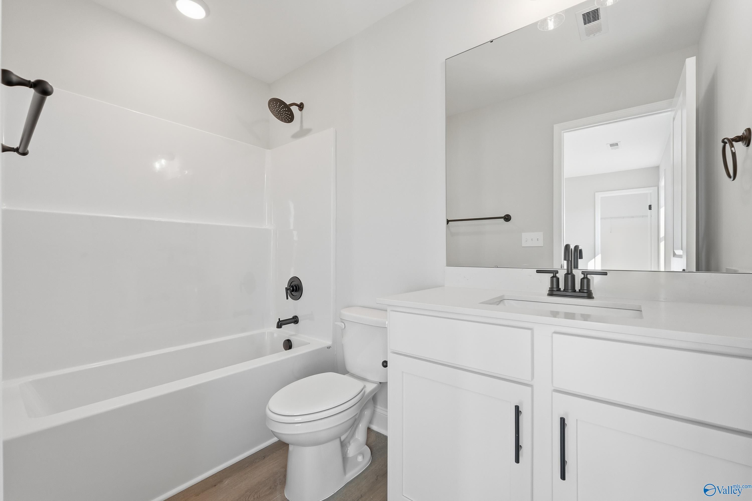 Bright white guest bathroom with bathtub, tiled shower, dual sink vanity, and bronze fixtures in Davidson Homes Chelsea C, Harvest AL