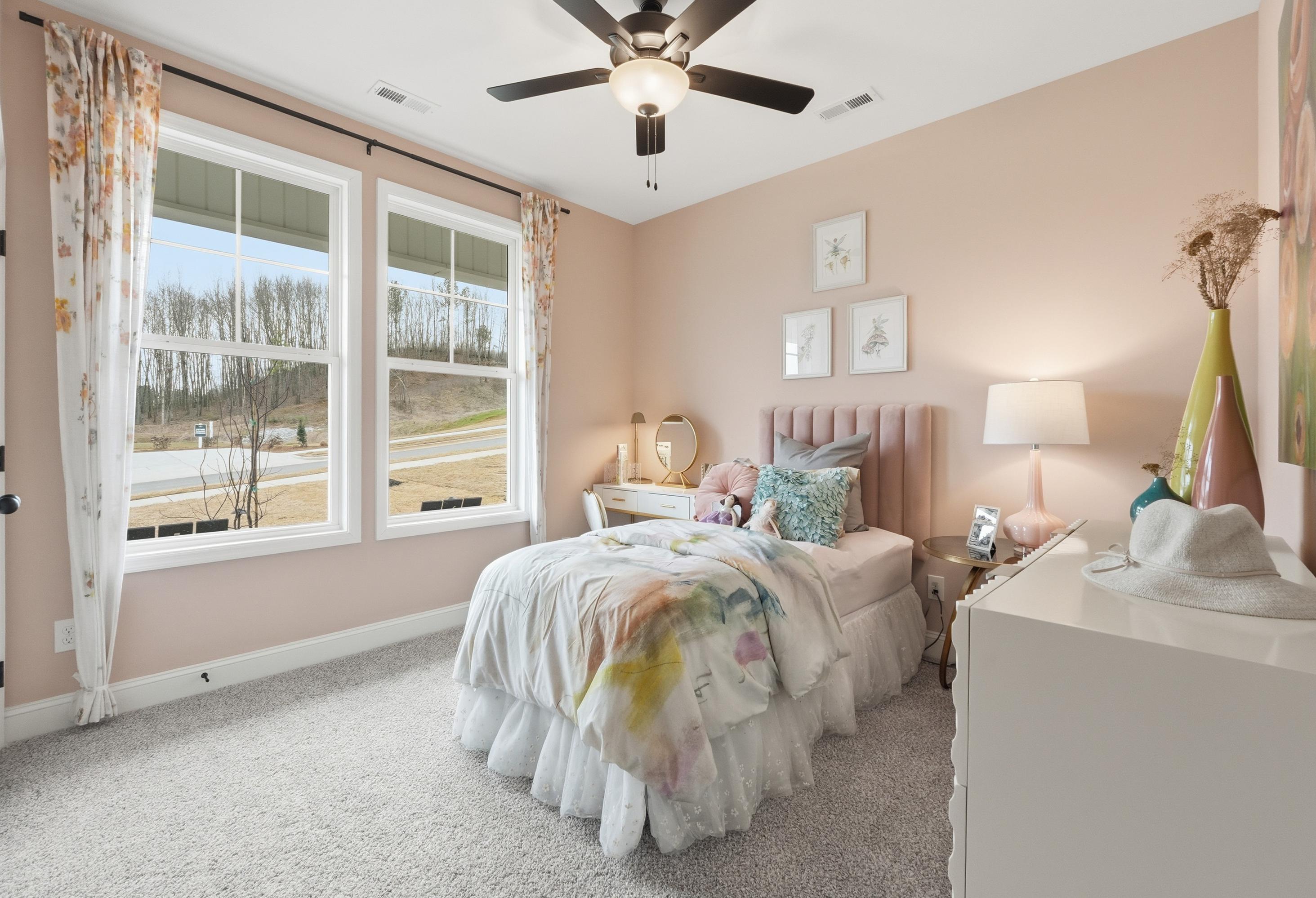 Cozy pastel bedroom in The Laurel home design with floral curtains, scenic wooded views, and whimsical decor