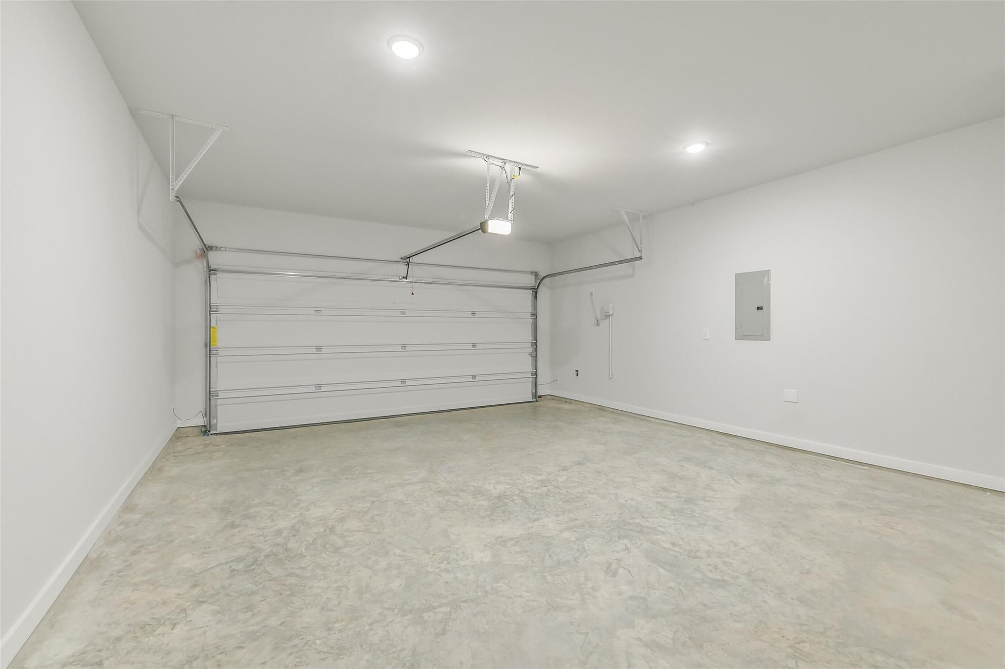 Spacious empty two-car garage with concrete floor, white walls, and overhead lights in Davidson Homes San Marcos E, Liberty Estates, Cleveland, Texas