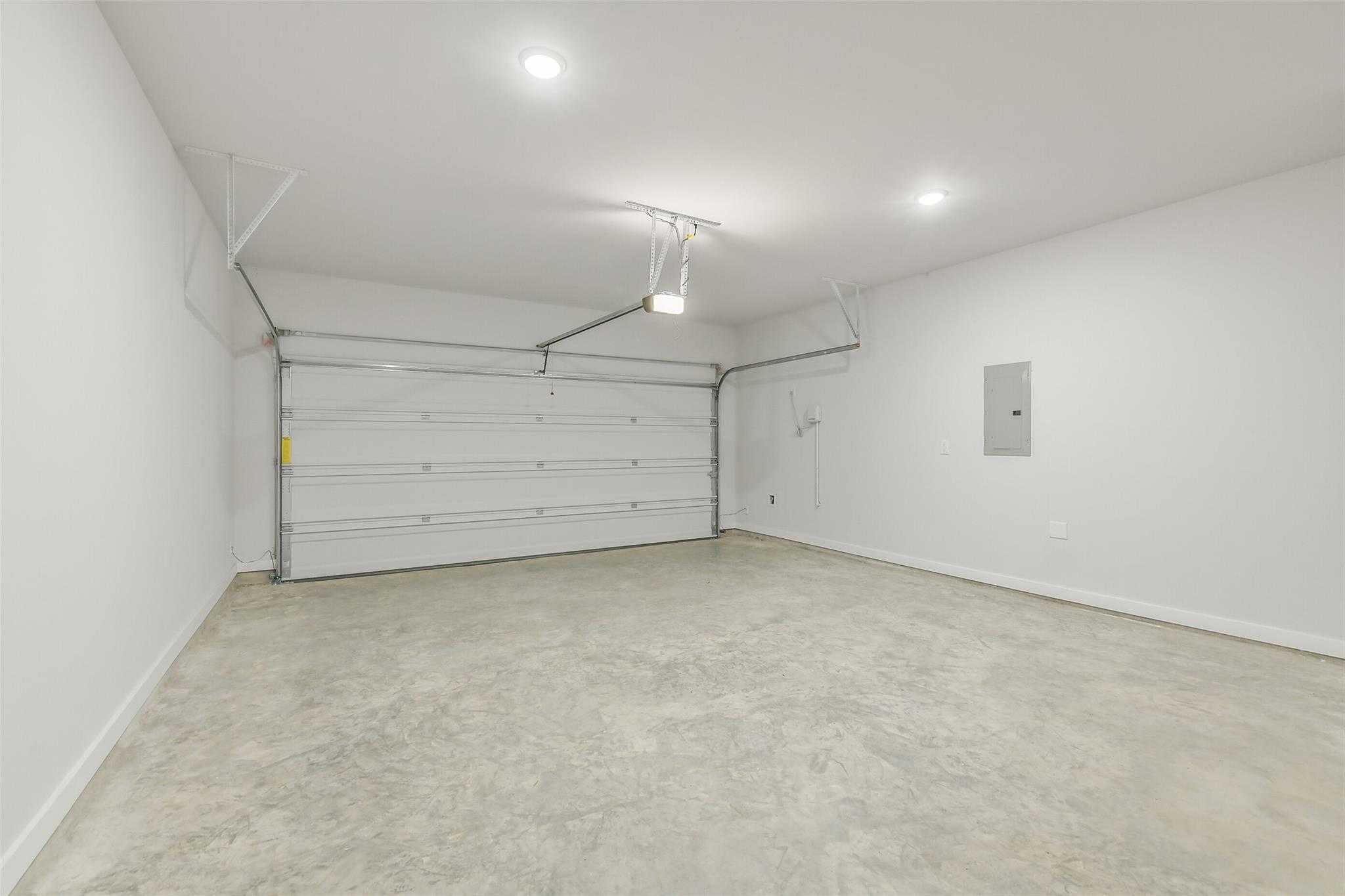 Spacious empty two-car garage with concrete floor, white walls, and overhead lights in Davidson Homes San Marcos E, Liberty Estates, Cleveland, Texas