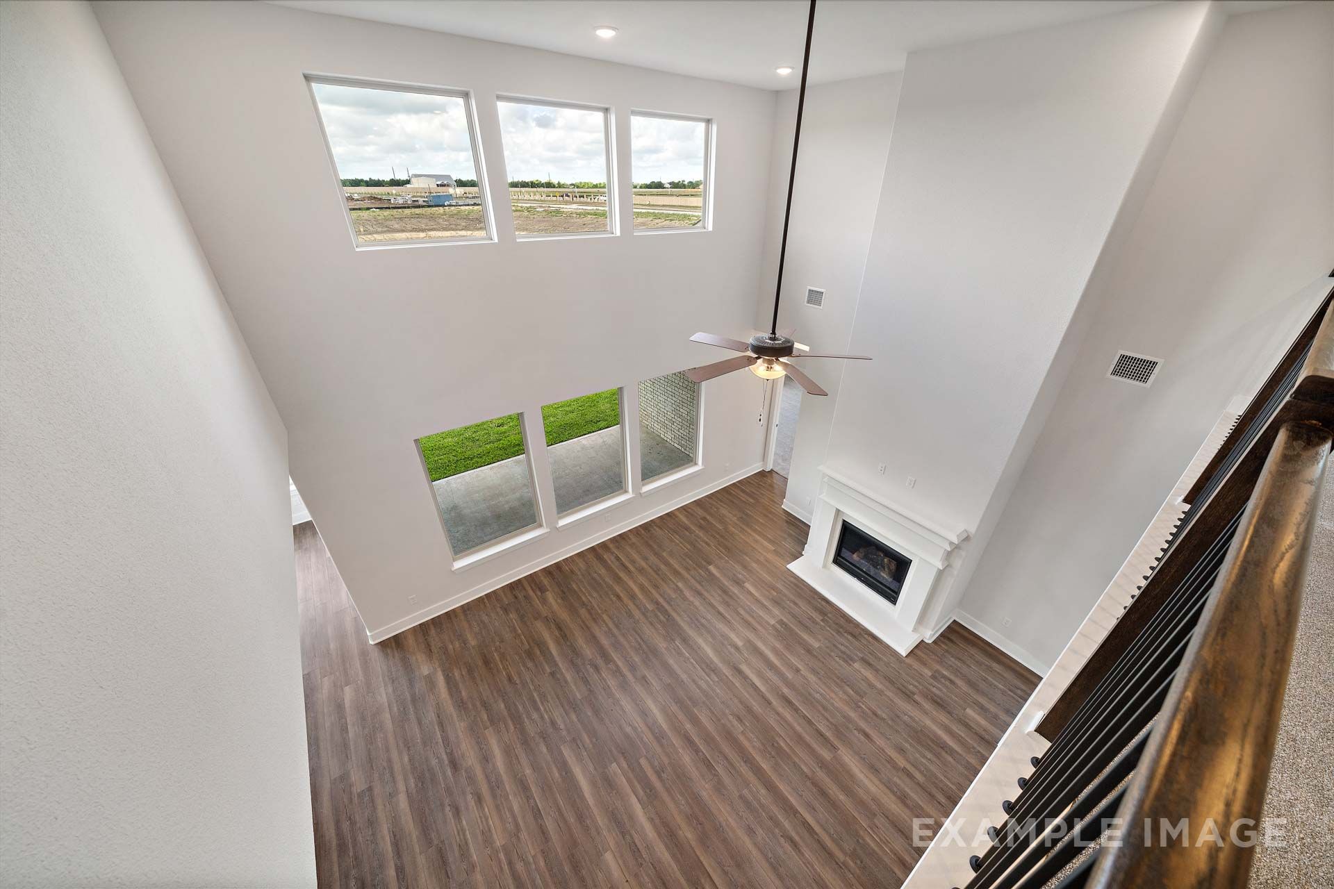 Two-story great room in The Victoria by Davidson Homes with fireplace, ceiling fan, hardwood floors, and tall windows.