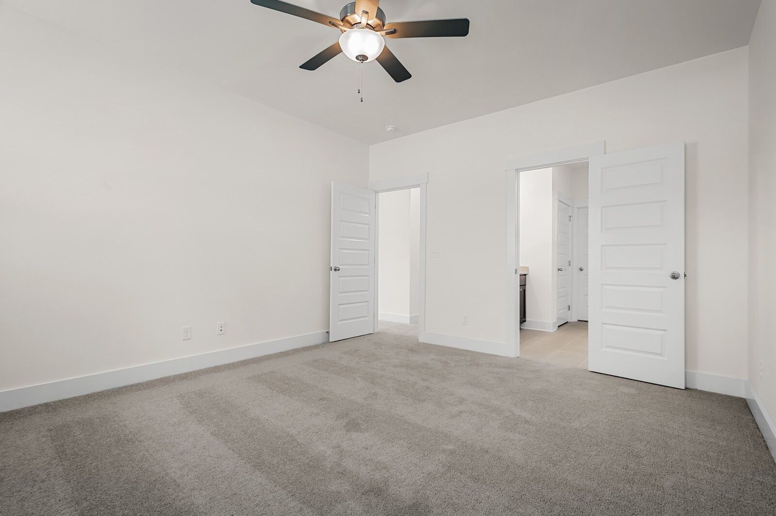 Spacious bedroom with grey carpet and ceiling fan in The Ash A floor plan at Woods Crossing in Gallatin, Tennessee.