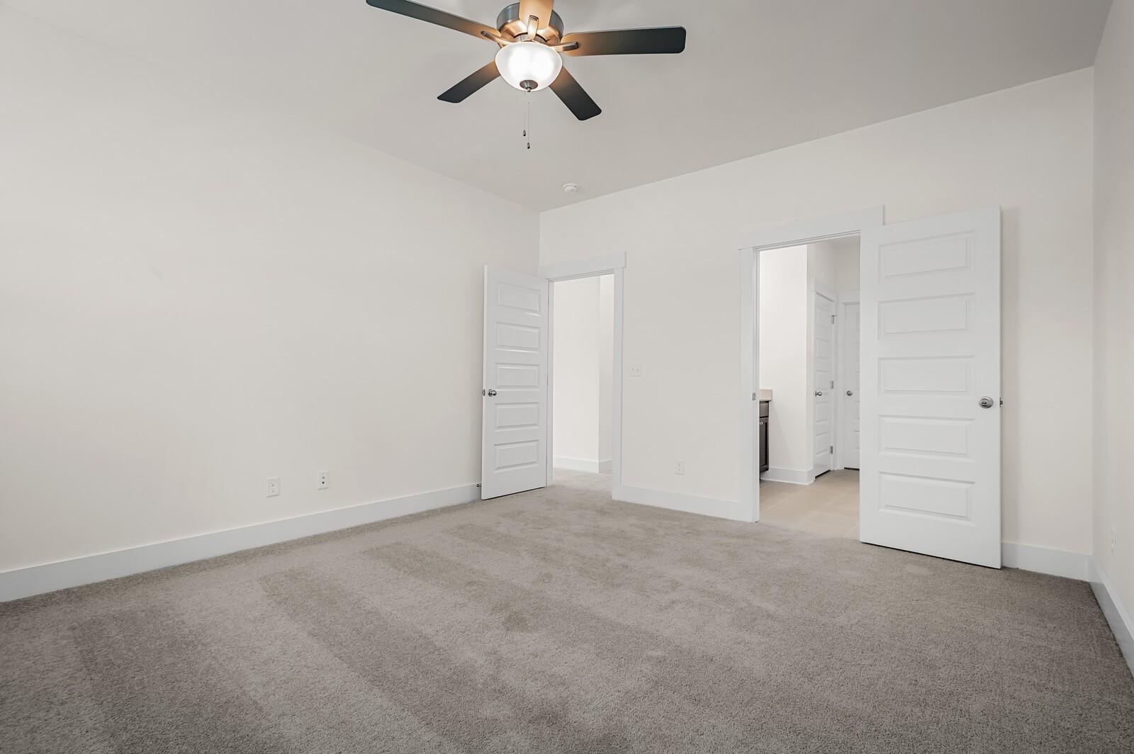 Spacious bedroom with grey carpet and ceiling fan in The Ash A floor plan at Woods Crossing in Gallatin, Tennessee.
