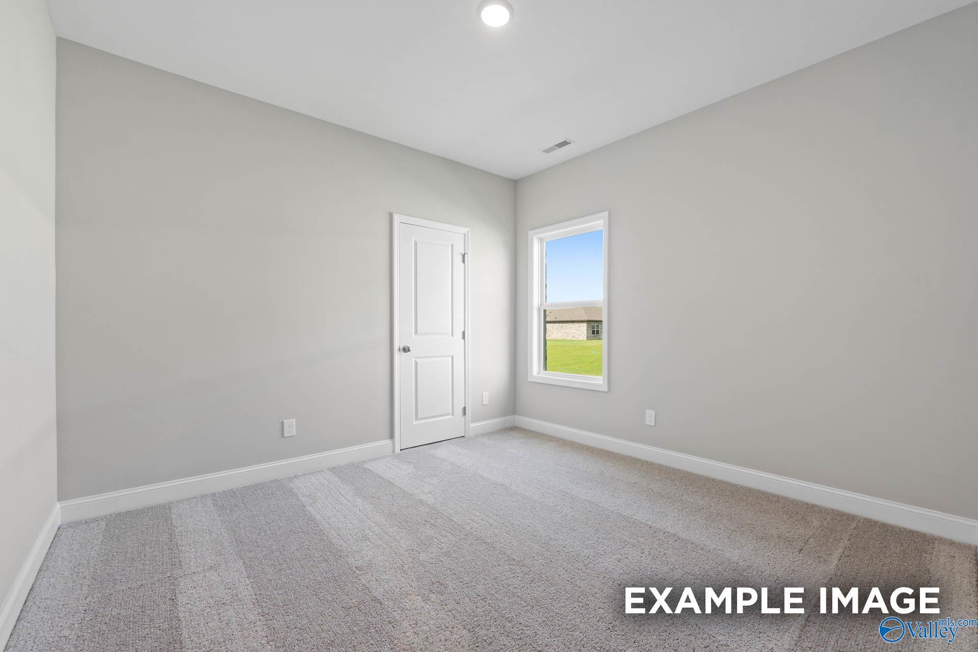 Bright secondary bedroom featuring gray walls, carpet floor, white door, and window with green yard view in The Everett B, Hazel Green, Alabama