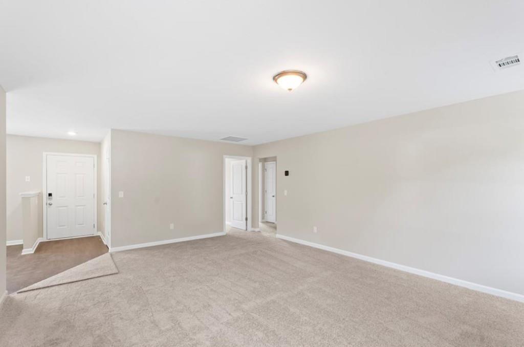 Spacious empty interior room with beige carpet, walls, white doors, and ceiling light in Davidson Homes The Washington, Phenix City, AL