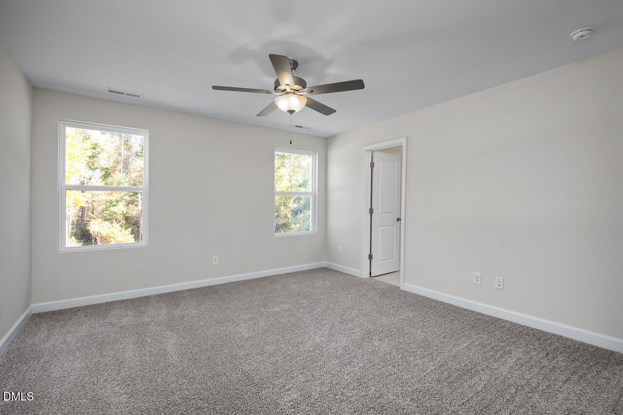 Bright secondary bedroom with neutral walls, plush carpet, ceiling fan, and large windows in Davidson Homes The Grace C, Lillington NC