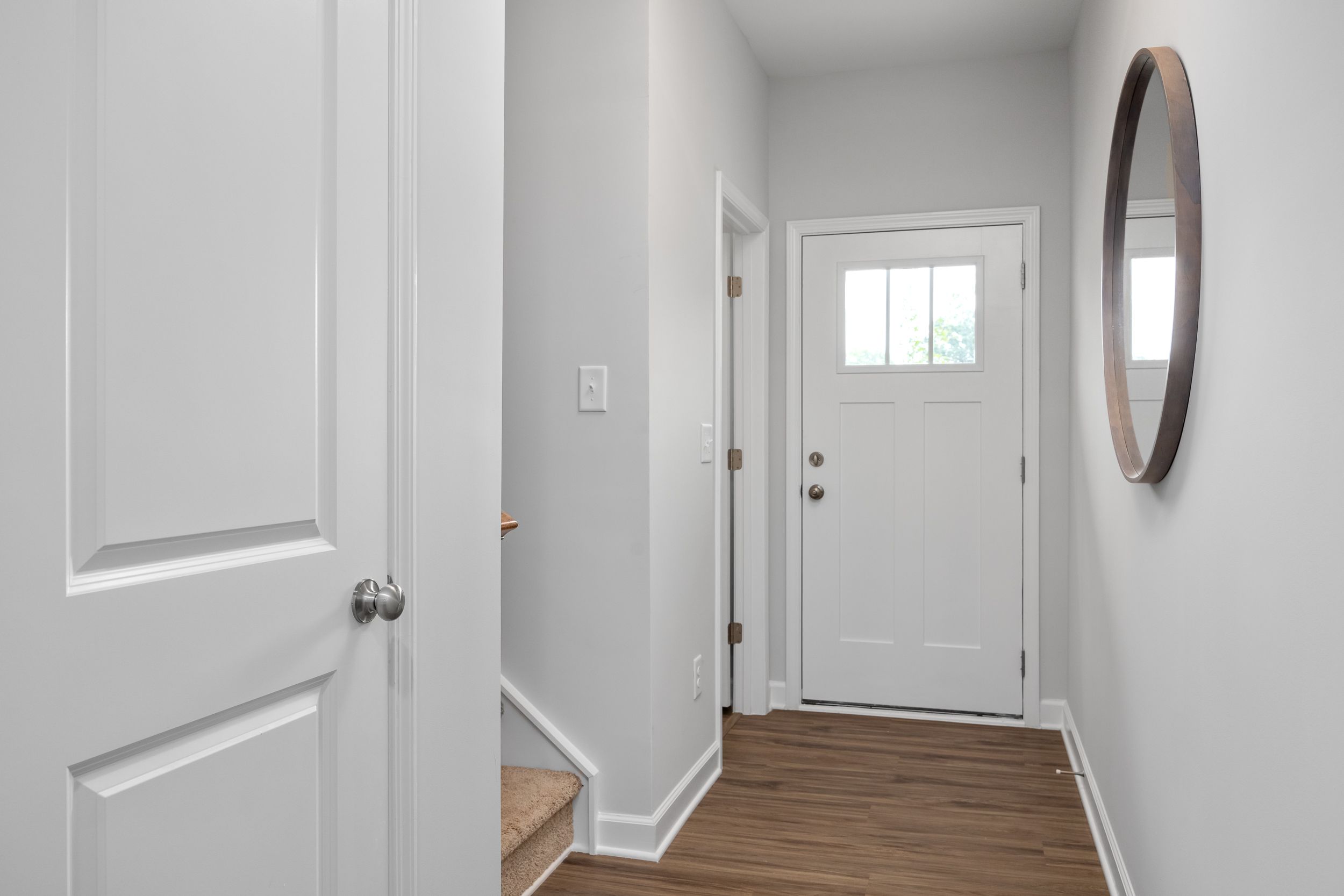 Bright entryway of The Warren by Davidson Homes featuring a white front door, wood flooring, and modern wall mirror.