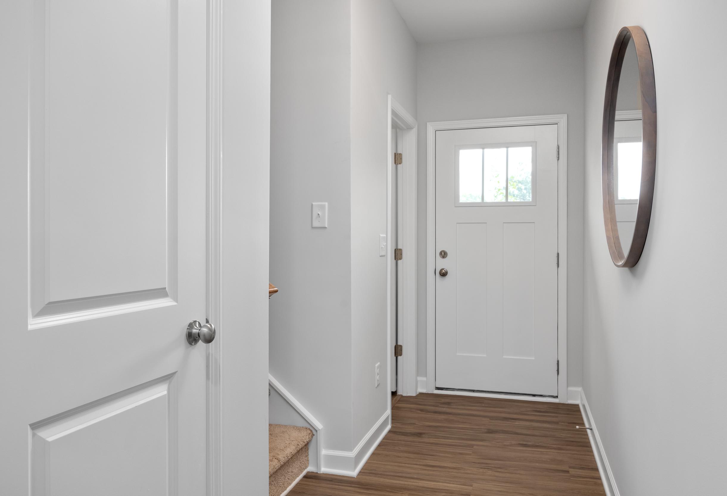 Bright entryway of The Warren by Davidson Homes featuring a white front door, wood flooring, and modern wall mirror.