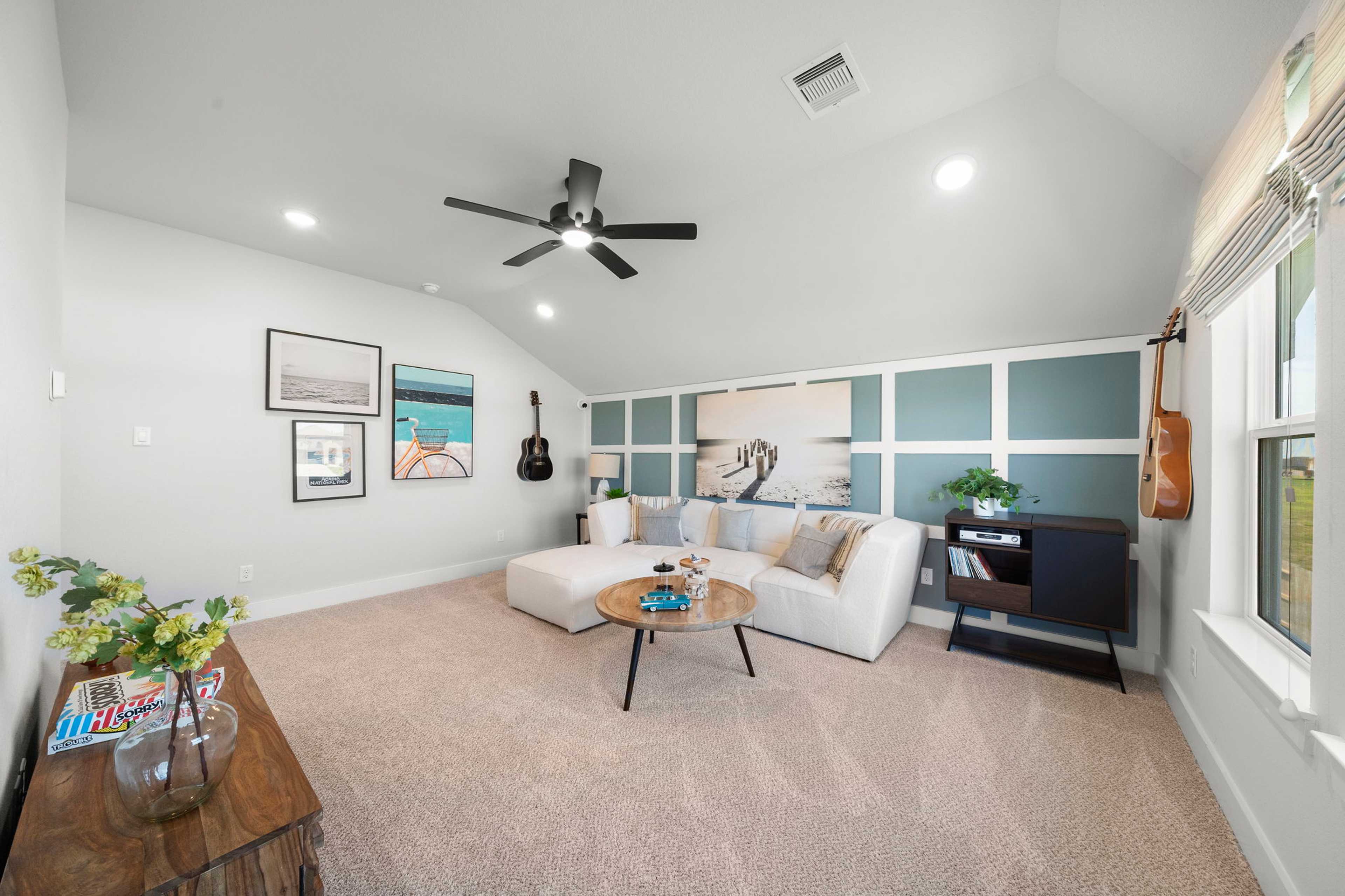 Spacious loft media room at Lago Mar in Texas City TX with white sectional sofa, beige carpet, ceiling fan, wall art and guitar accents