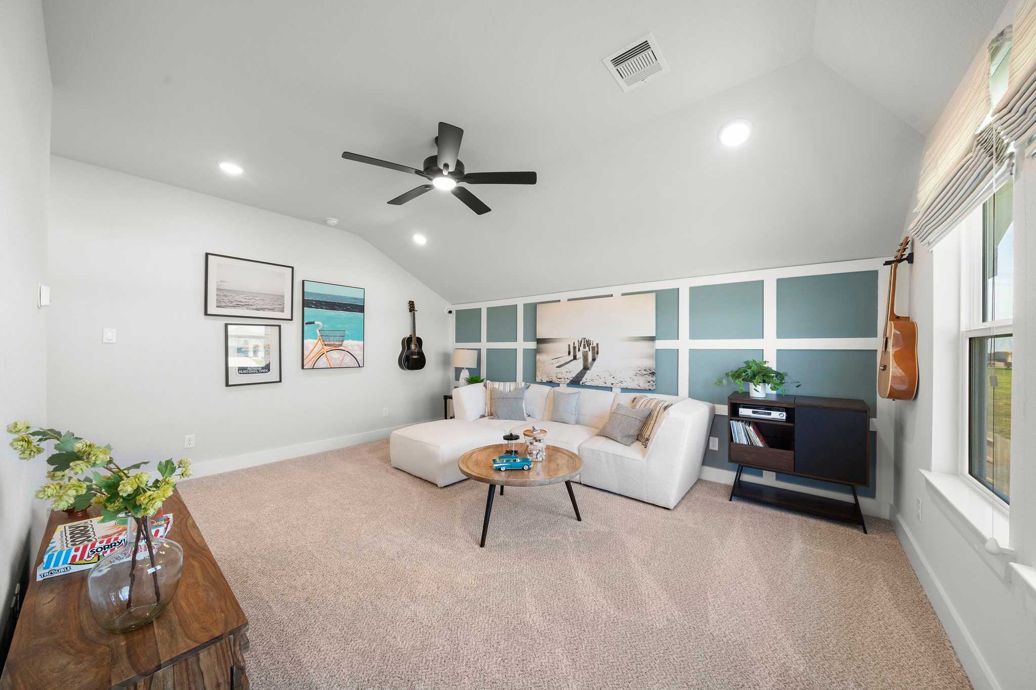 Spacious loft media room at Lago Mar in Texas City TX with white sectional sofa, beige carpet, ceiling fan, wall art and guitar accents