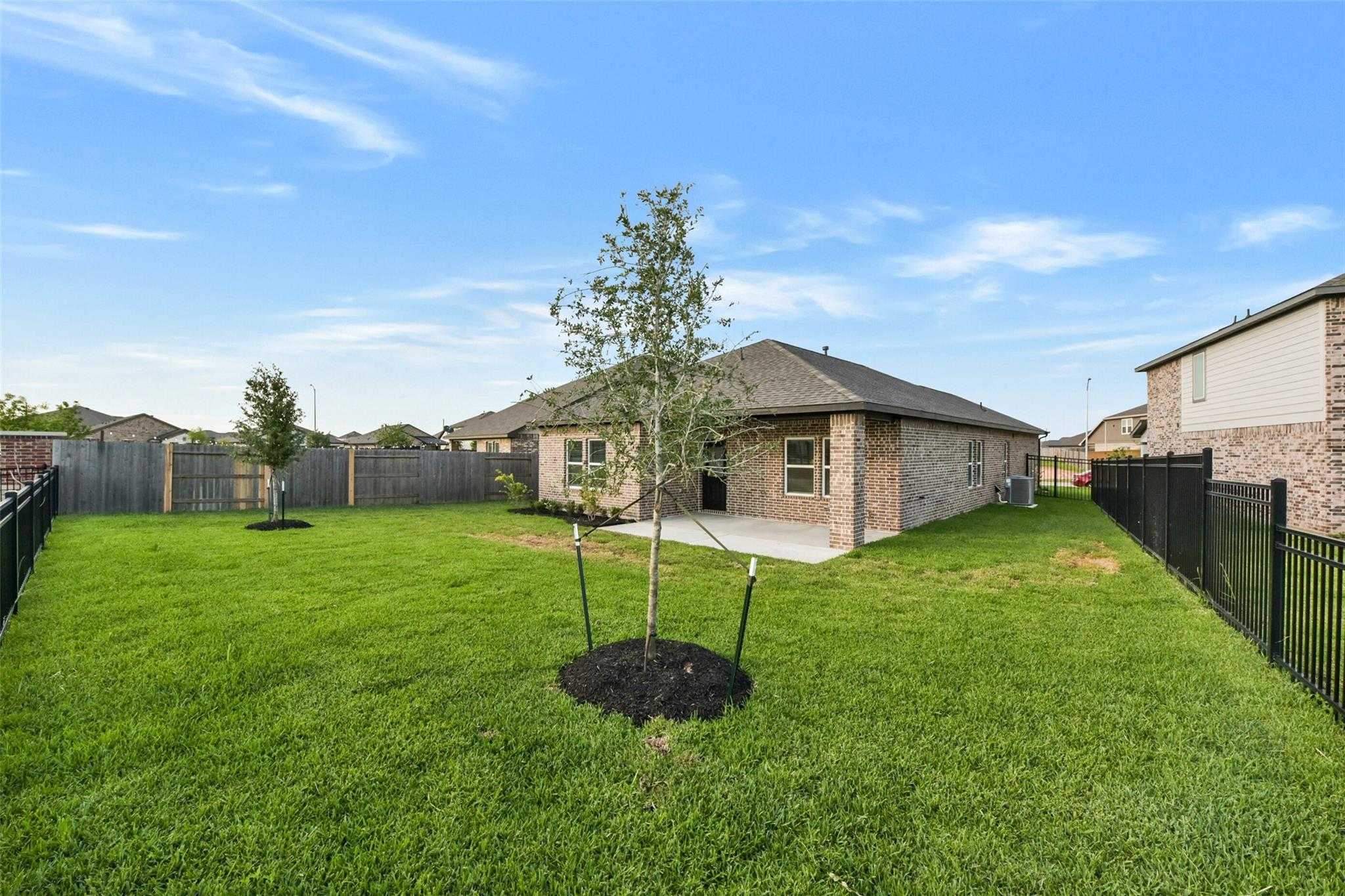 Spacious fenced backyard with green lawn, young trees, and brick garage in 3-bedroom Davidson Homes Laguna B, Sunterra, Katy, Texas