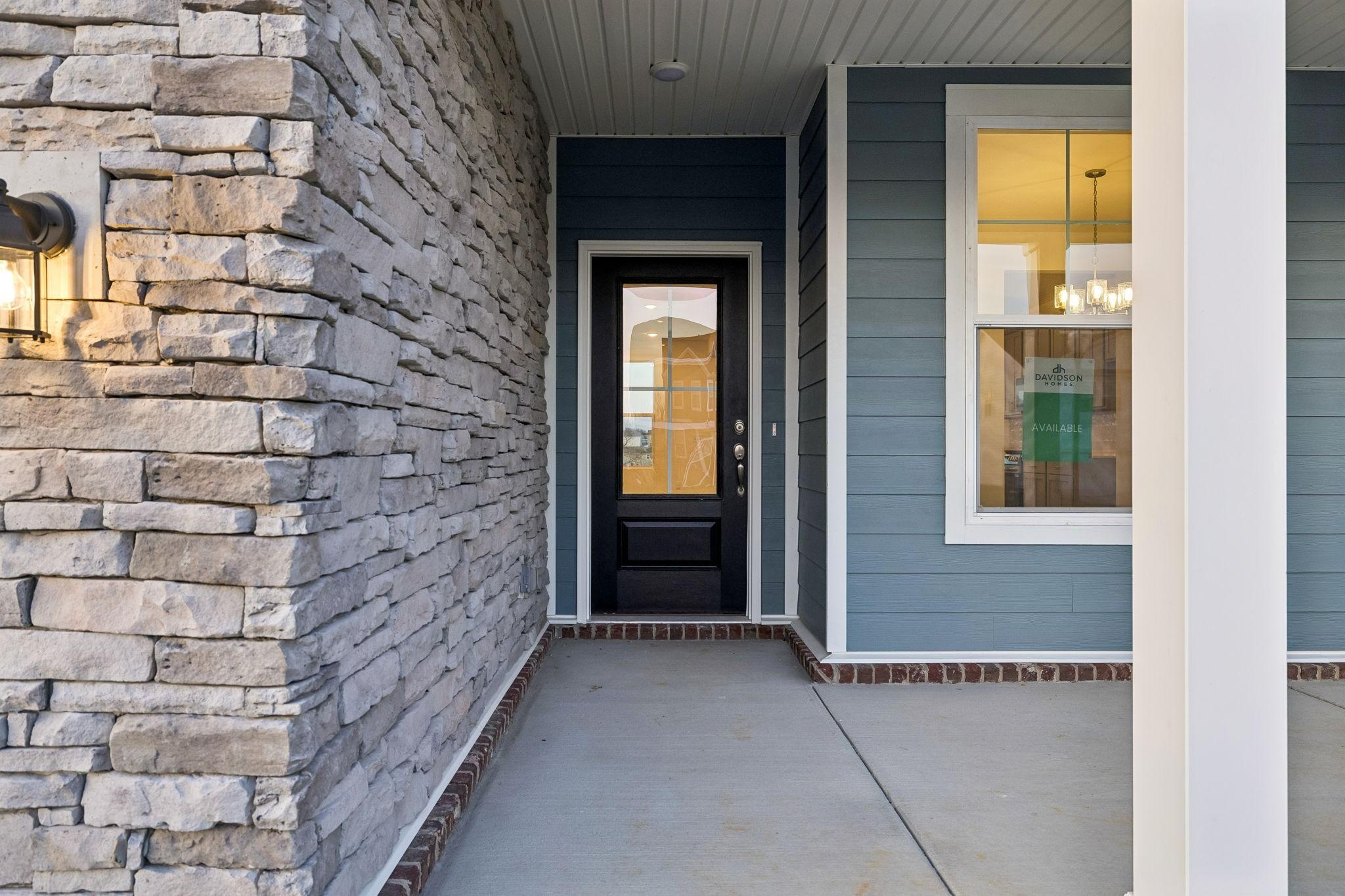 Modern front entrance featuring stone accents, blue siding, and glass-paneled black door on Davidson Homes The Willow in Calista Farms, White House, Tennessee