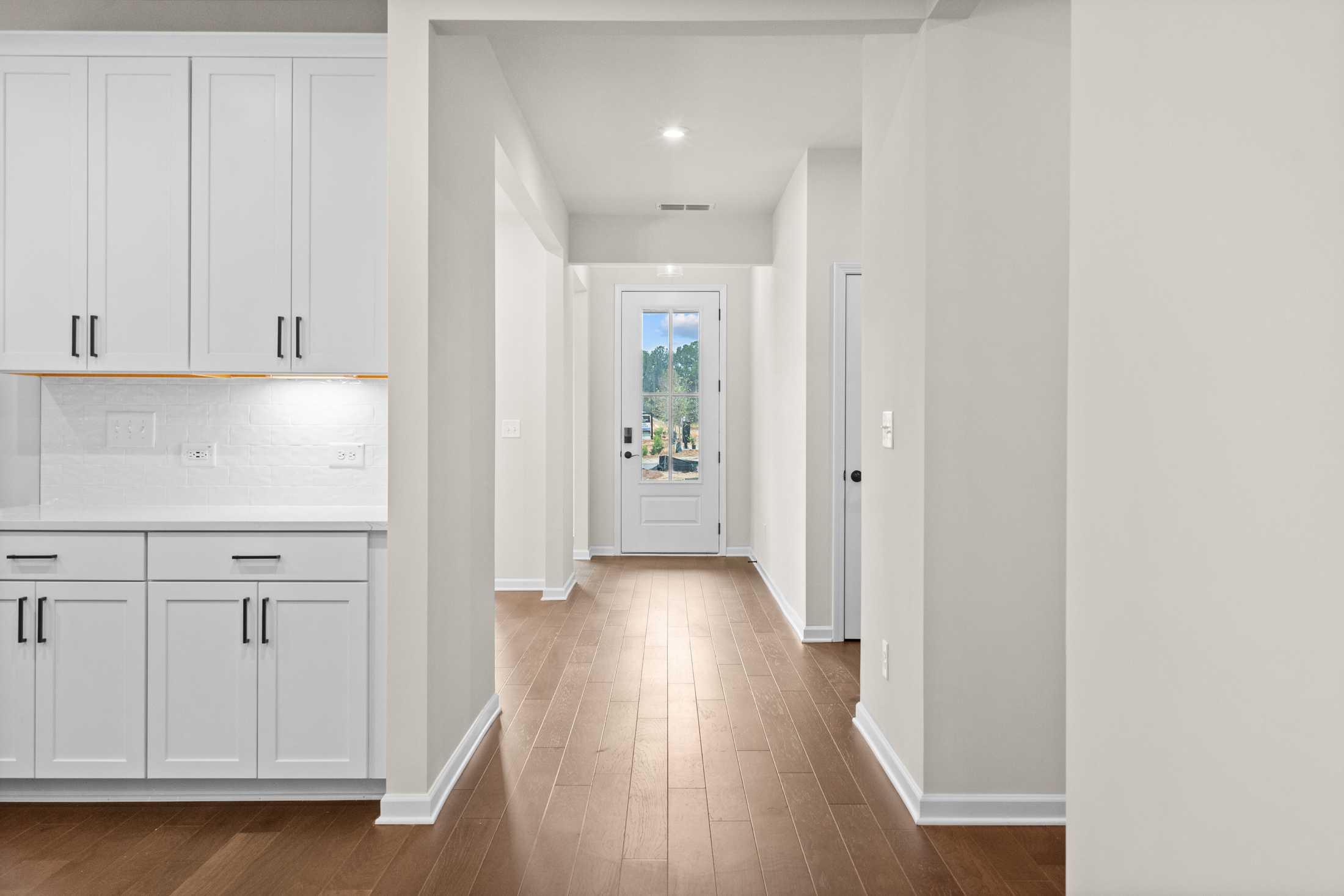 Spacious entry hallway in The Glenwood B showcasing white shaker cabinets, subway tile backsplash, hardwood floors, and glass-paneled front door