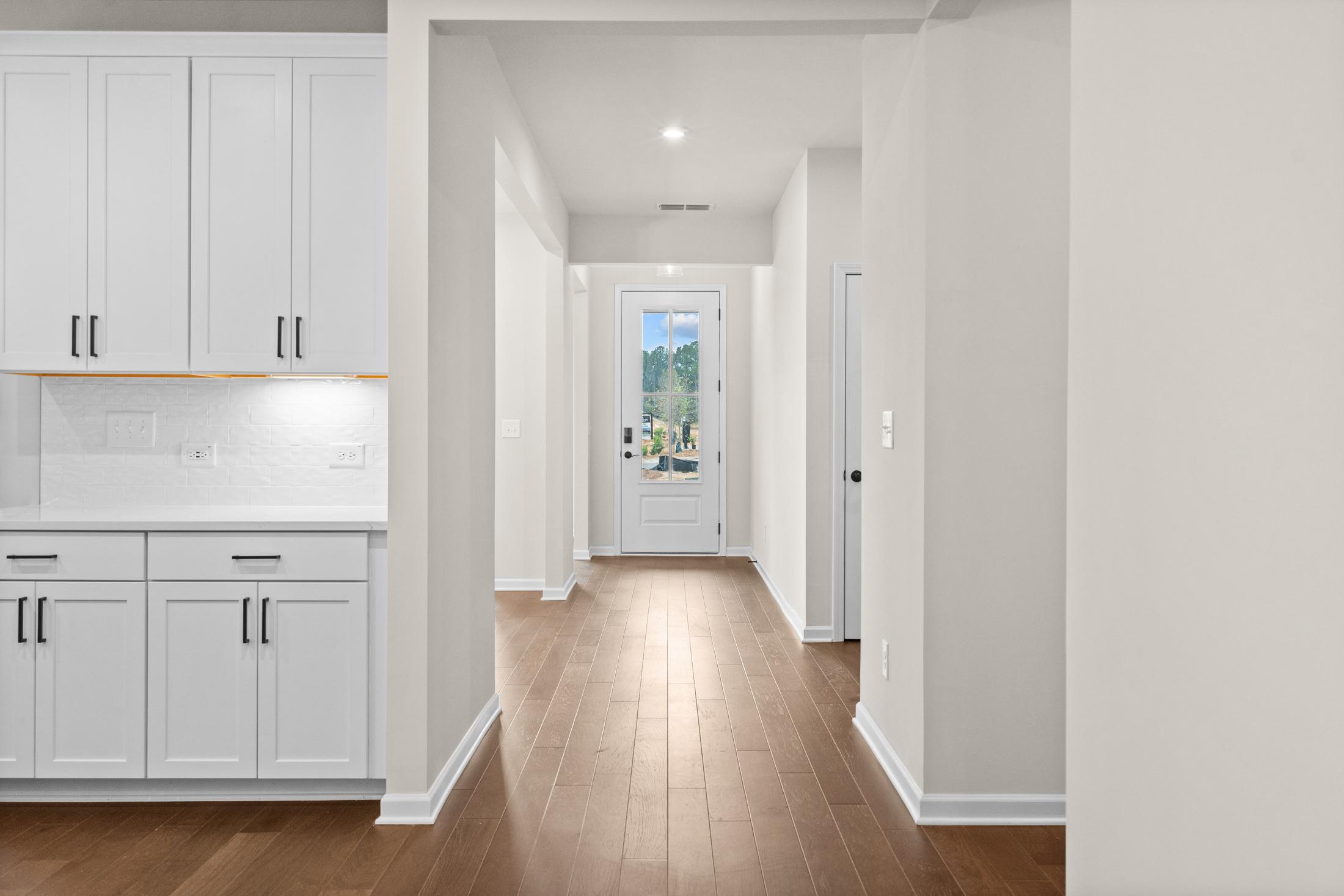Spacious entry hallway in The Glenwood home with white shaker cabinets, hardwood floors, and glass-paneled front door