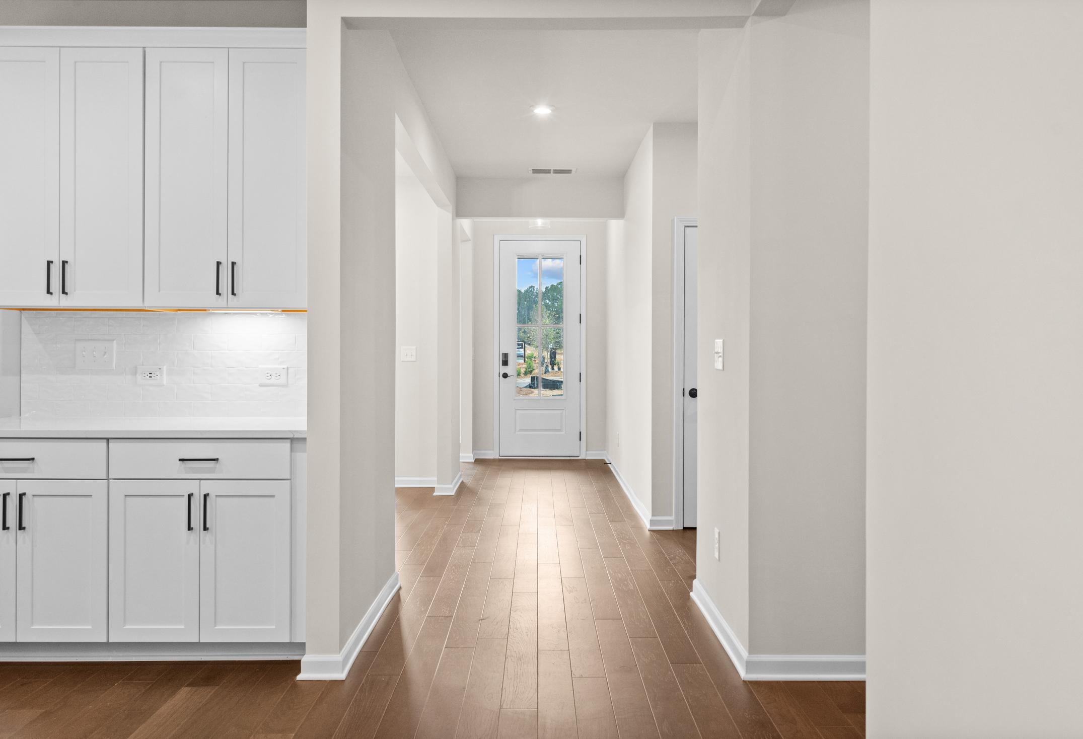 Spacious entry hallway in The Glenwood home with white shaker cabinets, hardwood floors, and glass-paneled front door