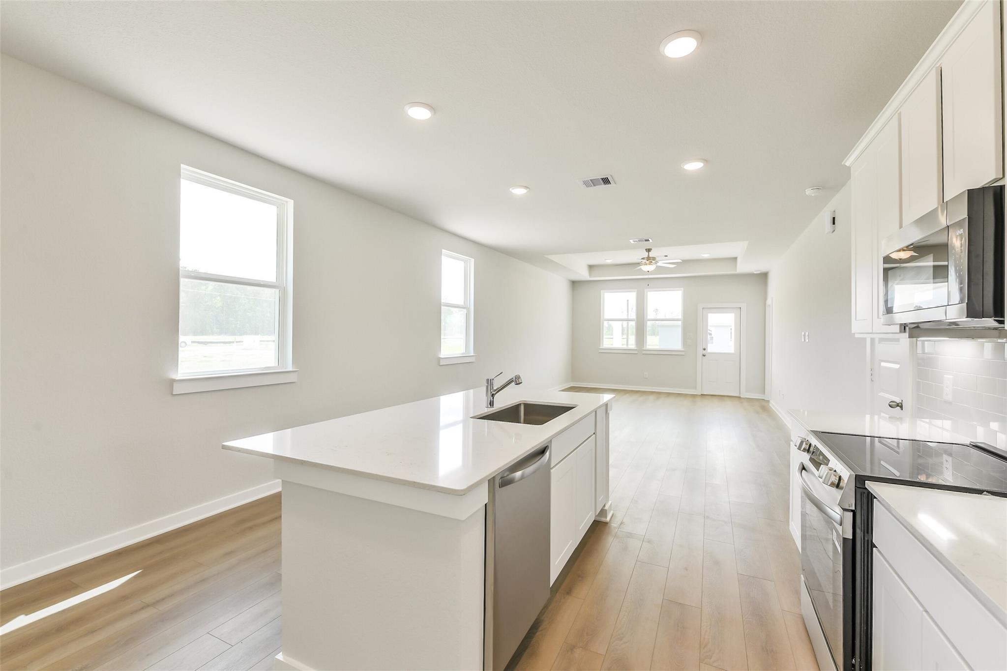 Modern kitchen with white quartz island, stainless steel appliances, and open living space in The Frio G home, Conroe, TX