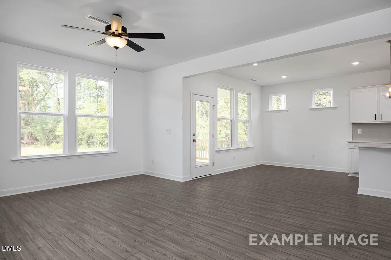 Open living room with ceiling fans, large windows, and adjacent kitchen in The Willow D by Davidson Homes, Zebulon, NC
