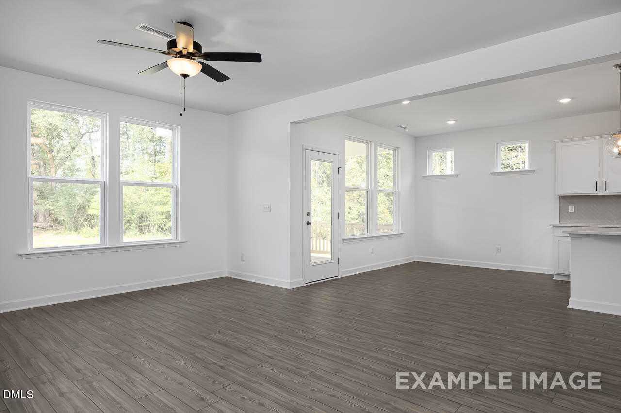 Open living room with ceiling fans, large windows, and adjacent kitchen in The Willow D by Davidson Homes, Zebulon, NC
