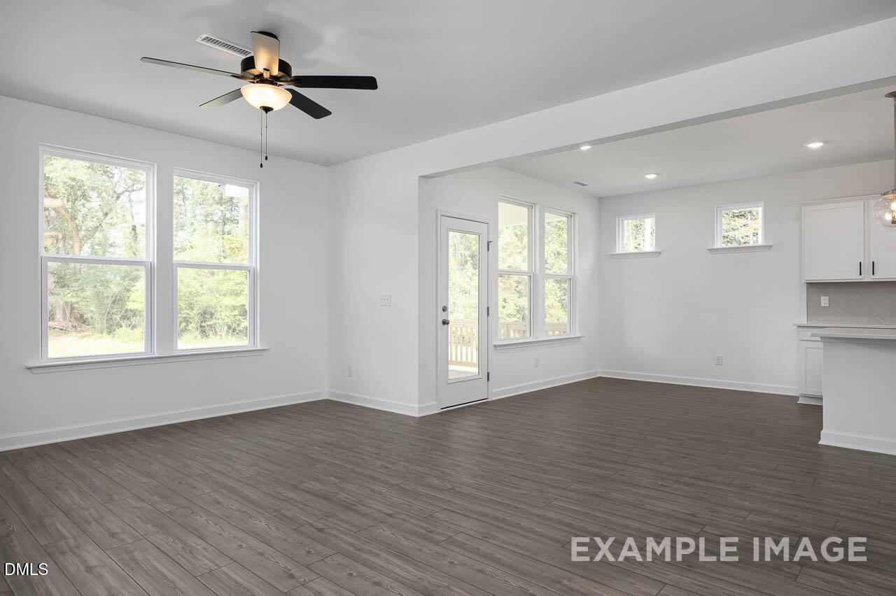 Bright open-concept living room with hardwood floors, ceiling fans, large windows, and adjacent kitchen in The Willow D by Davidson Homes, Zebulon, NC