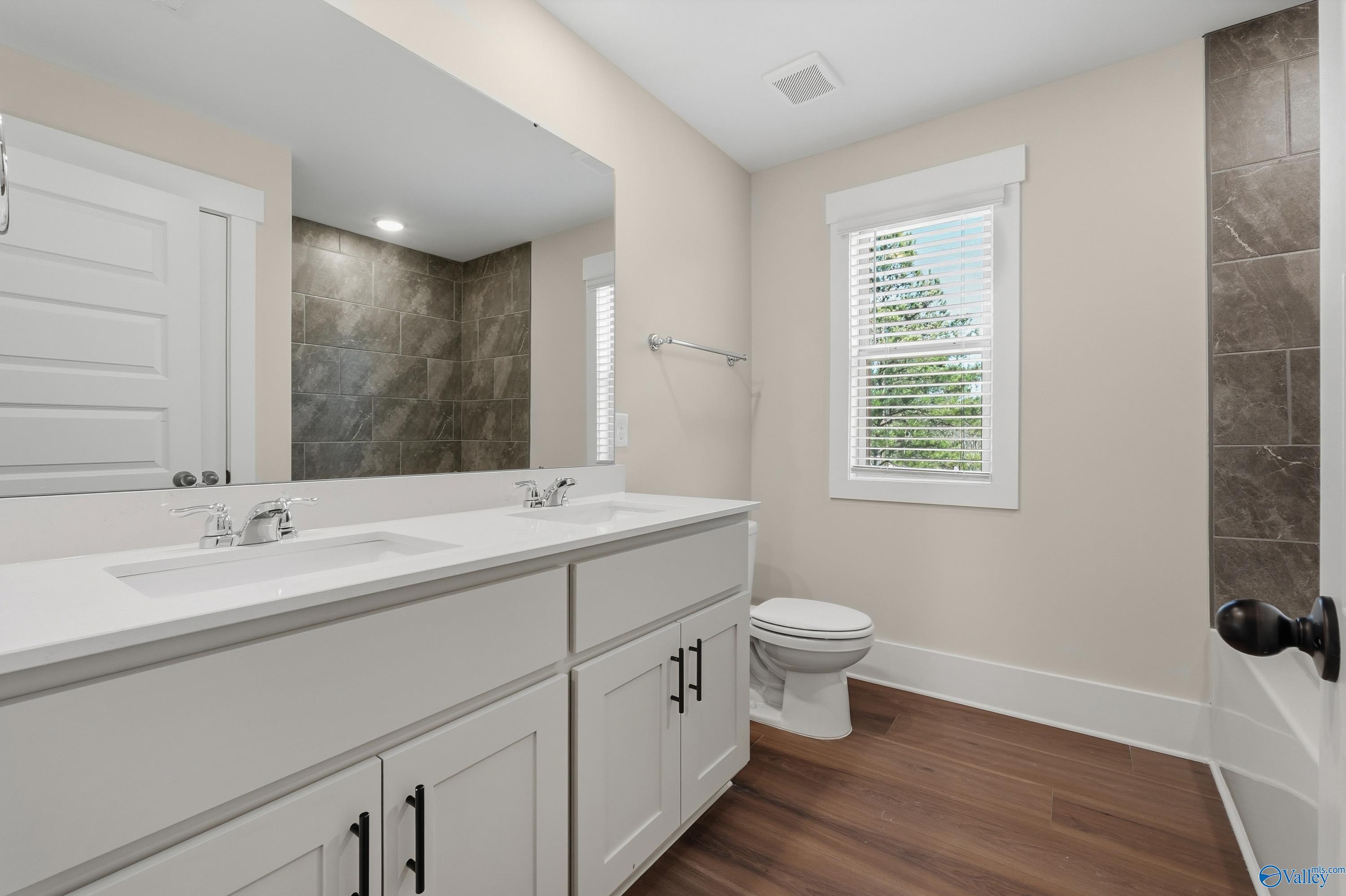 Modern master bathroom with double vanity, large mirror, wood floors, and stone accent in Davidson Homes Shelby A, Athens, AL
