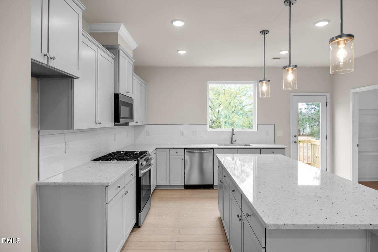 Modern white shaker kitchen with quartz island, stainless appliances, subway tile backsplash, and deck view in Davidson Homes The Avery, Knightdale NC