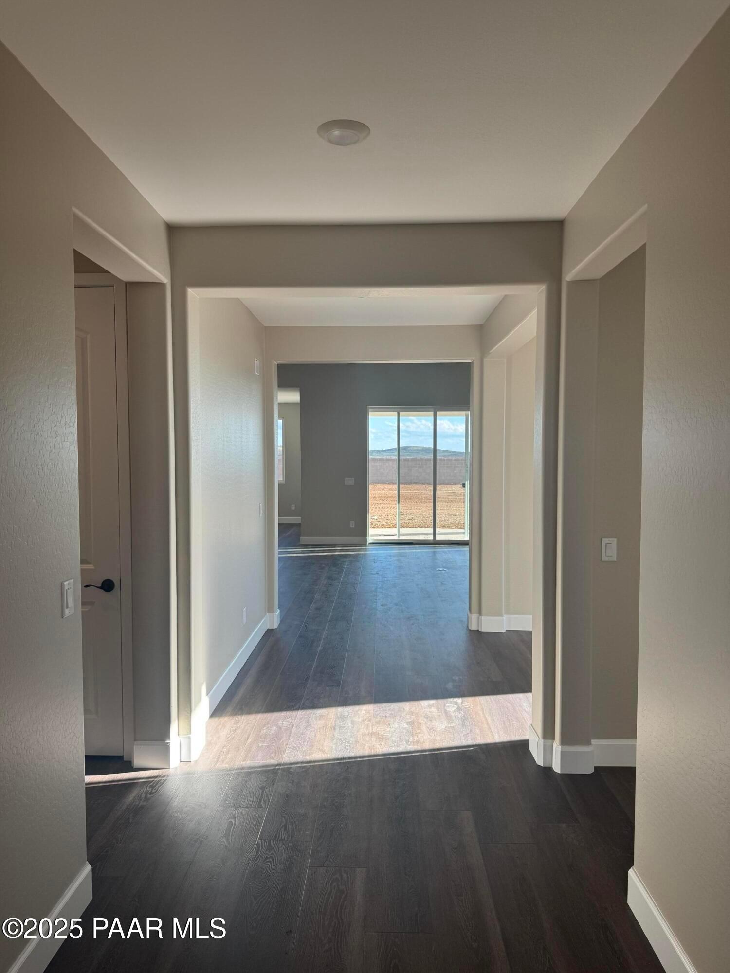 Bright hallway with dark hardwood floors, arched doorways, and desert mountain views through large windows in Evermore Homes The Sunrise A, Prescott Valley, Arizona