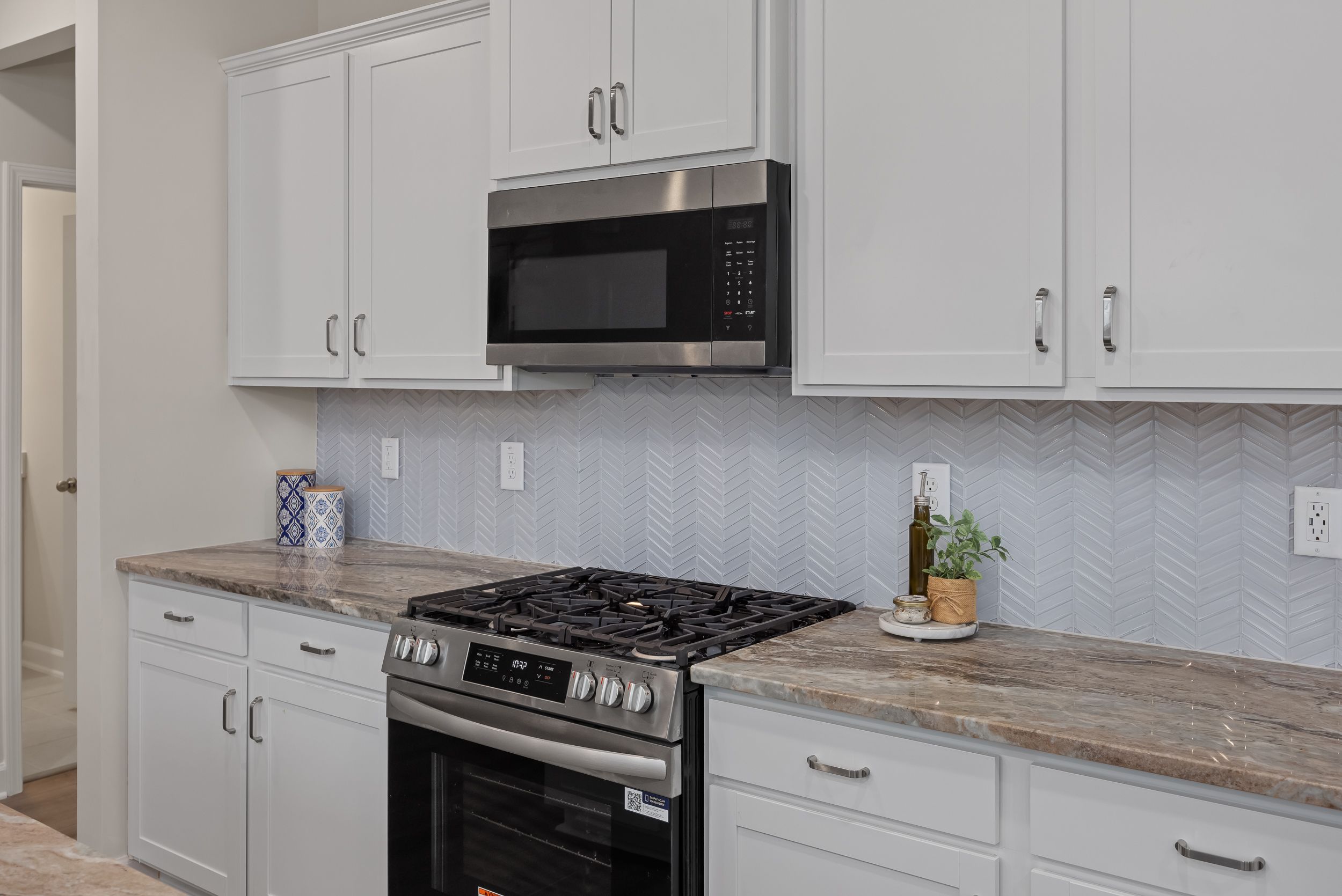 Modern kitchen at Gregory Village in Lillington, NC featuring white cabinets, stone countertops, and herringbone backsplash.