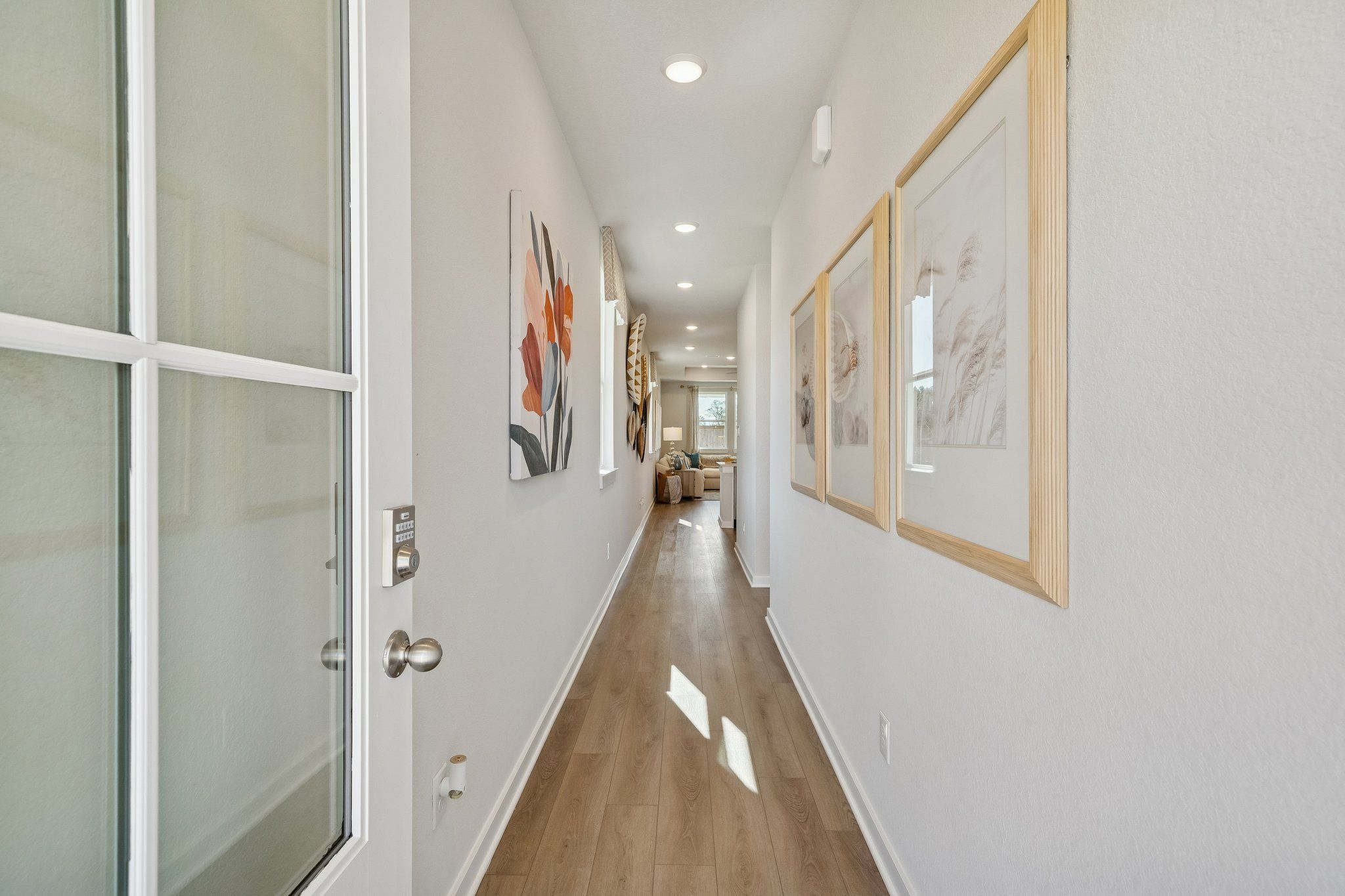 Bright hallway with light hardwood floors, recessed lighting, and abstract wall art at Spring Branch Crossing in Conroe, Texas