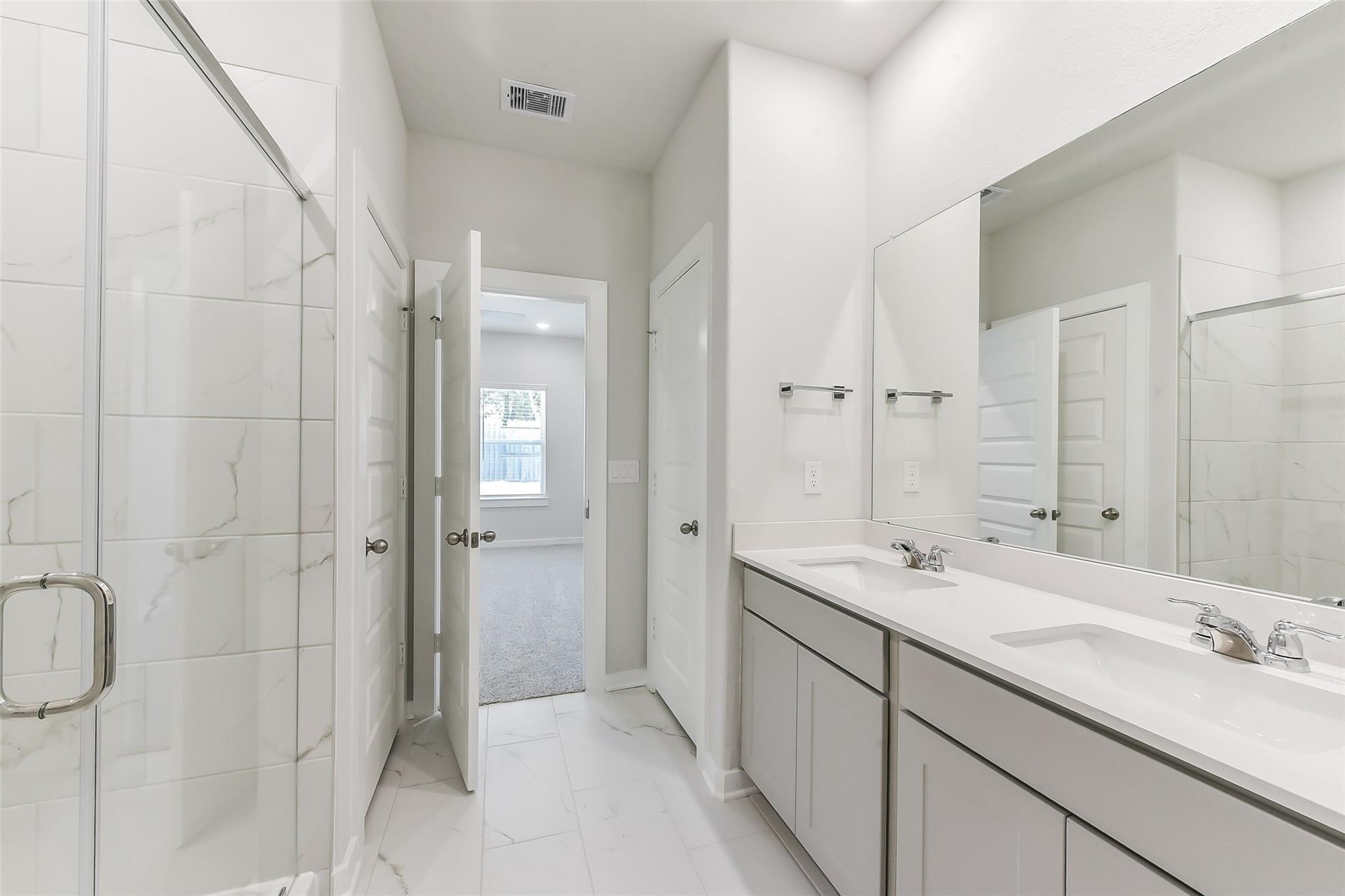 Modern master bathroom with frameless glass shower, double vanity sinks, and white tiled floors in Davidson Homes The Brazos E, Magnolia, Texas