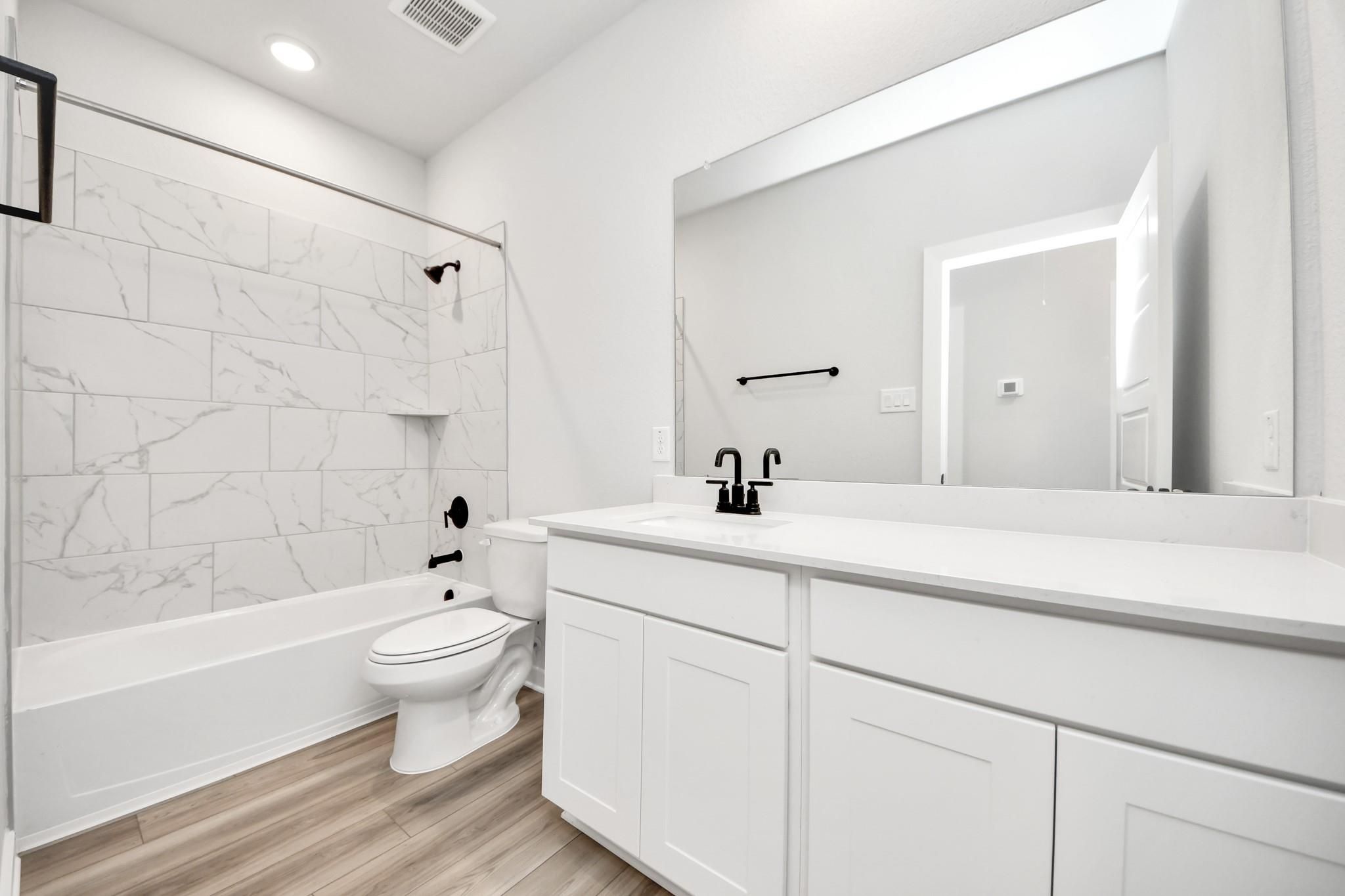 Modern bathroom with marble-look tub surround and white vanity in The Sorrento E floor plan at Sundance Cove, Crosby, TX.