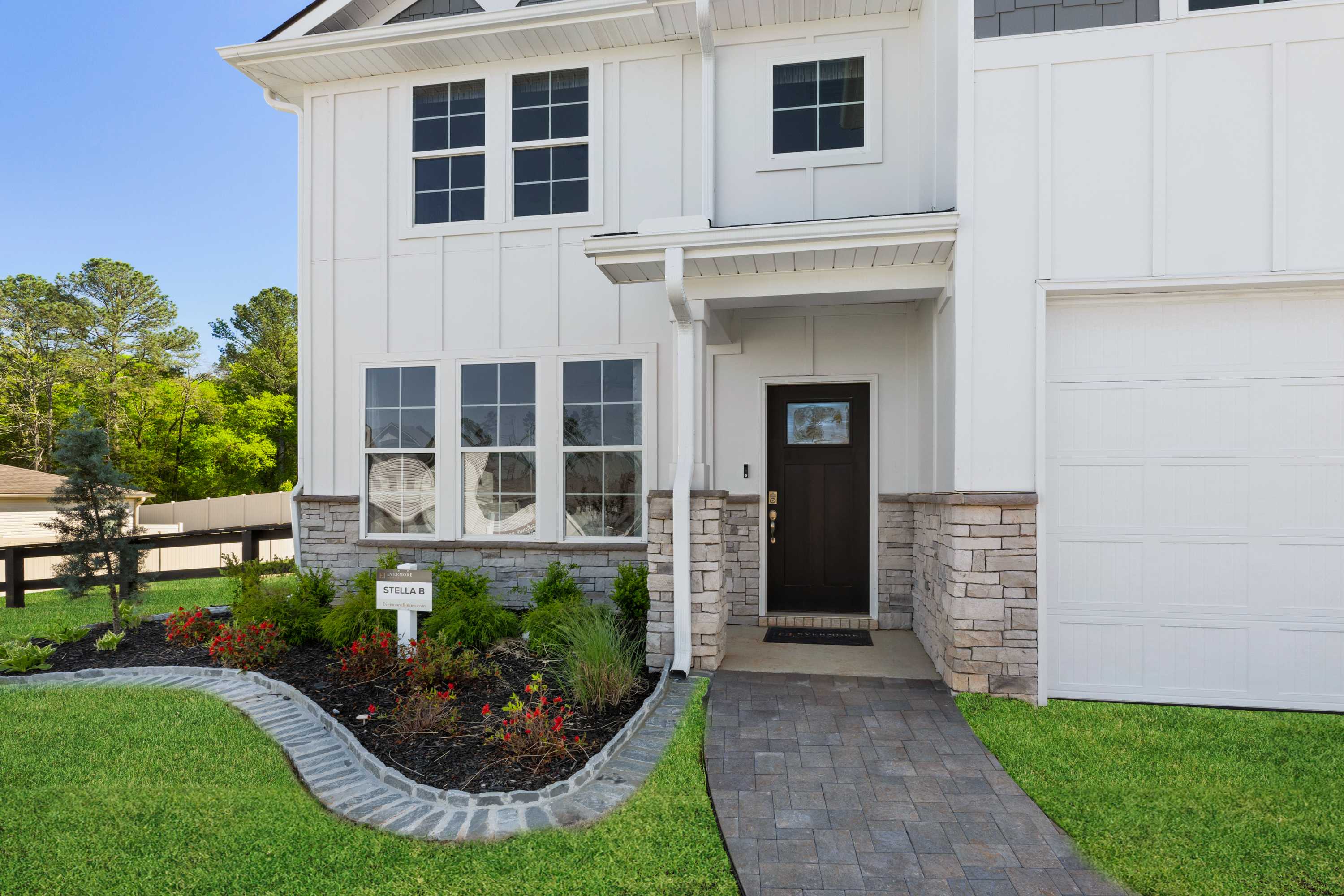 Modern white-sided home exterior at Evergreen Mill in Madison, Alabama with covered porch, stone accents, and landscaped flower beds