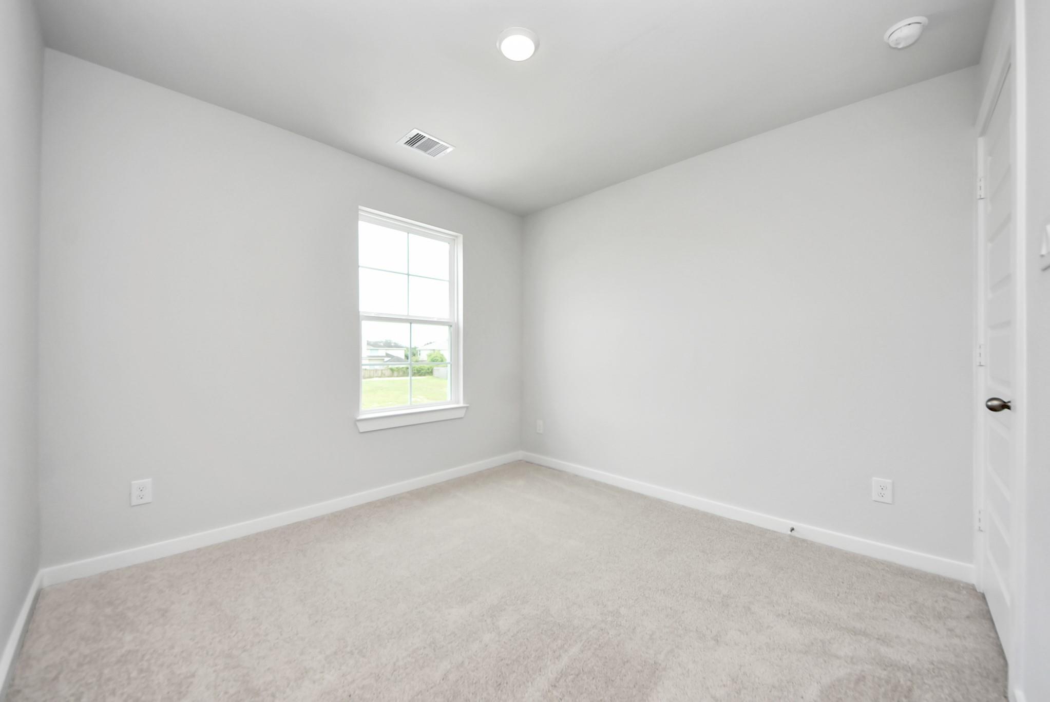 Bright, carpeted bedroom with neutral walls in The Blanco E floor plan at The Villages at WestPointe in Dayton, Texas.