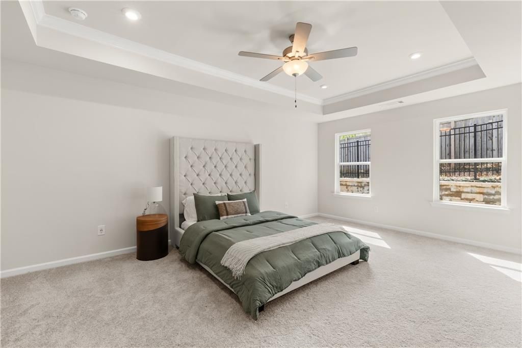 Elegant master bedroom with tufted gray headboard, green bedding, ceiling fan, and large windows in Davidson Homes The Marion B, Kennesaw, GA