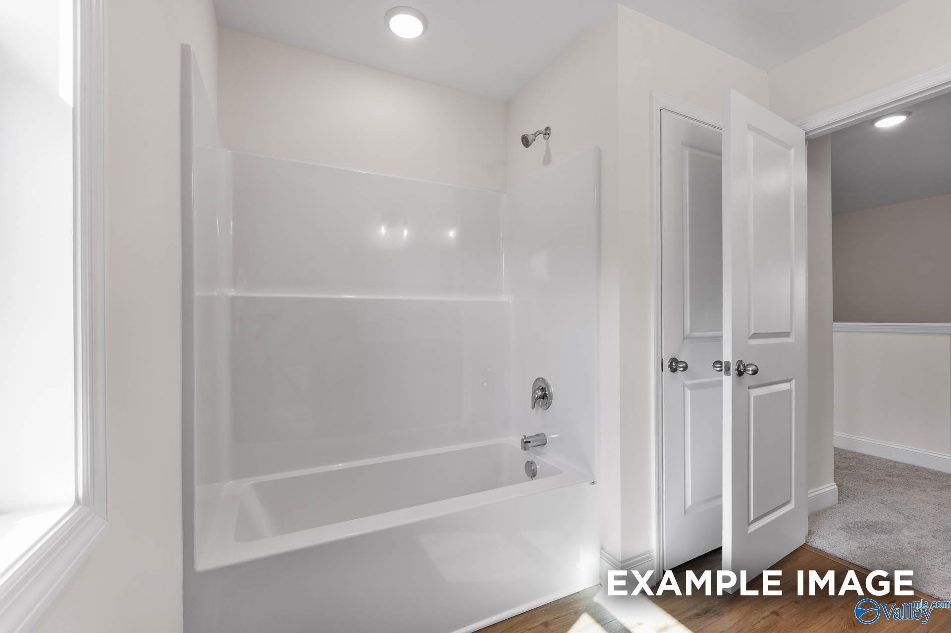 Modern bathroom with white tiled walk-in shower, deep soaking tub, and open closet doors in Davidson Homes The Shelby A, Hazel Green AL