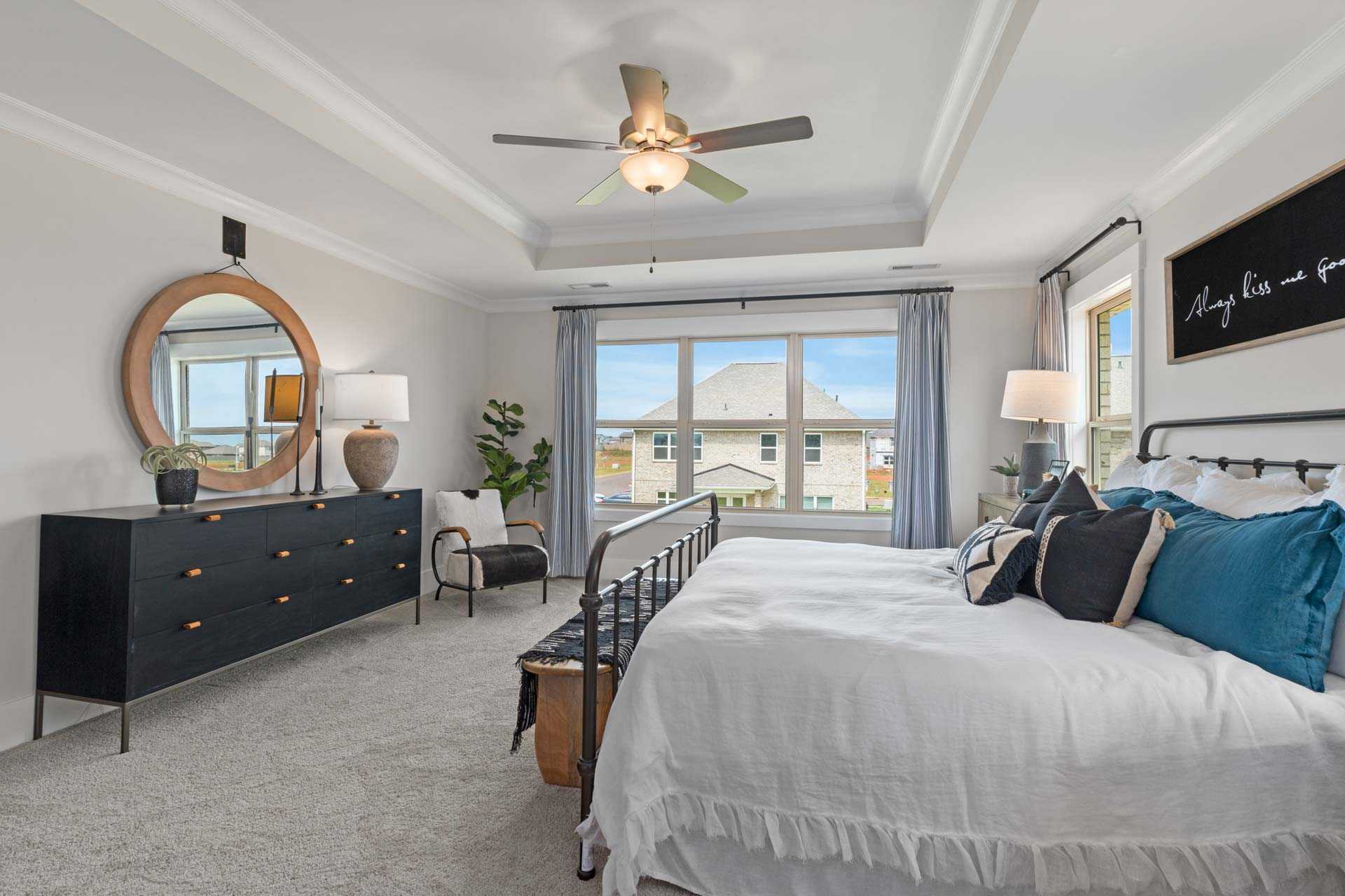 Spacious master bedroom at Walker's Hill in Meridianville, Alabama with black iron bed, plush white bedding, ceiling fan, and neighborhood window view