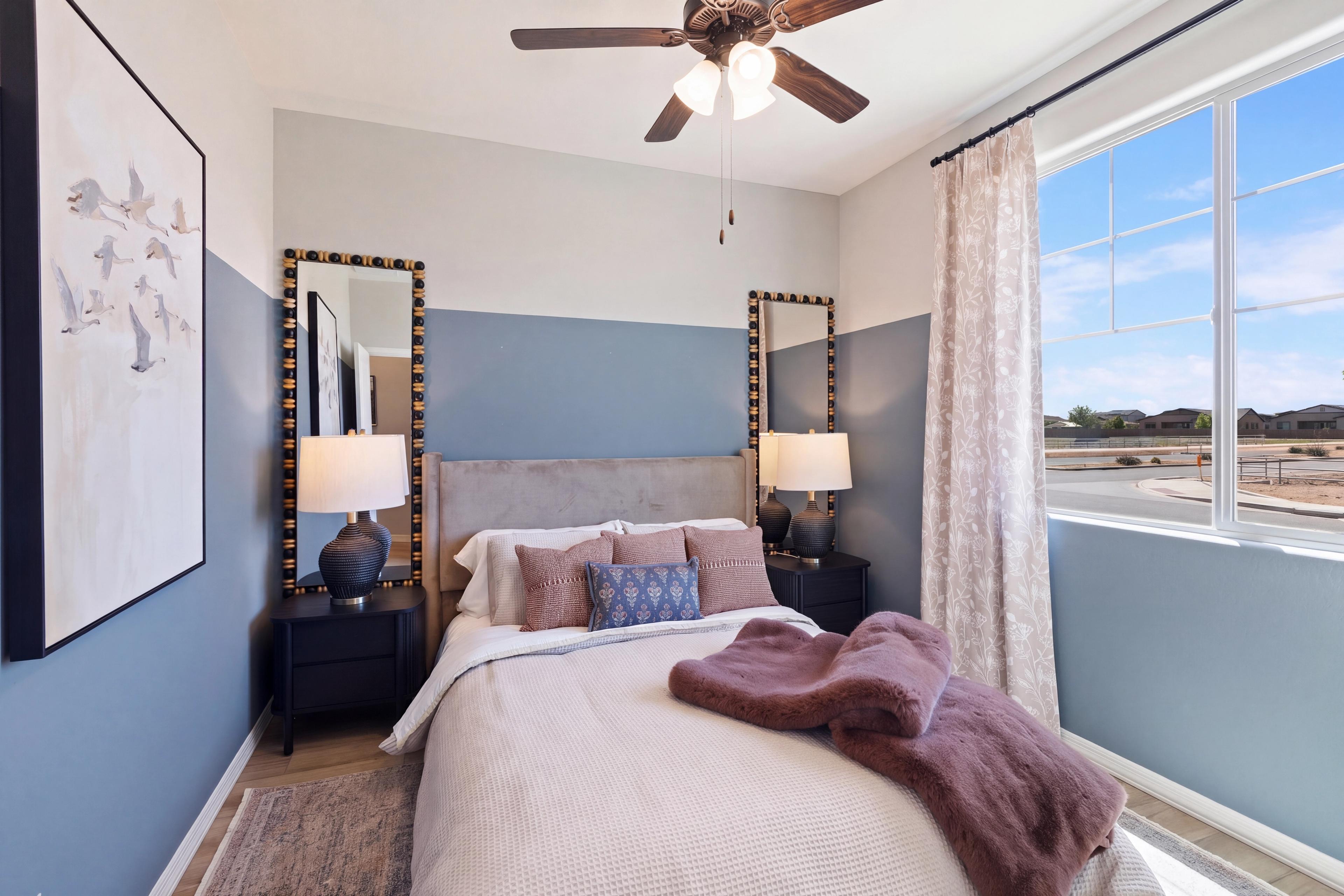Cozy bedroom with blue accent wall, upholstered bed, beaded mirrors, bird artwork, and large window at North Ridge Pronghorn Ranch in Prescott Valley AZ