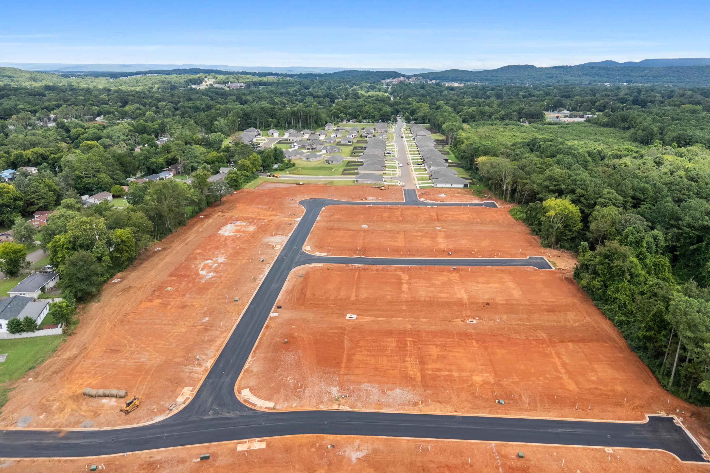 Aerial view of red clay home lots and paved streets at Blue Spring in Huntsville Alabama surrounded by green forests