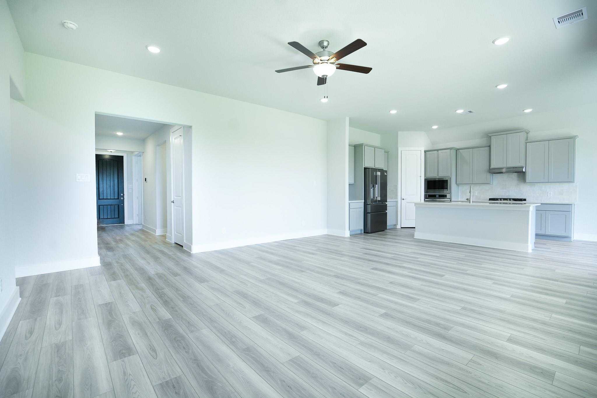 Spacious open-concept living and kitchen with white cabinets, stainless appliances, ceiling fan in Davidson Homes Edward A, Lago Mar, Texas City